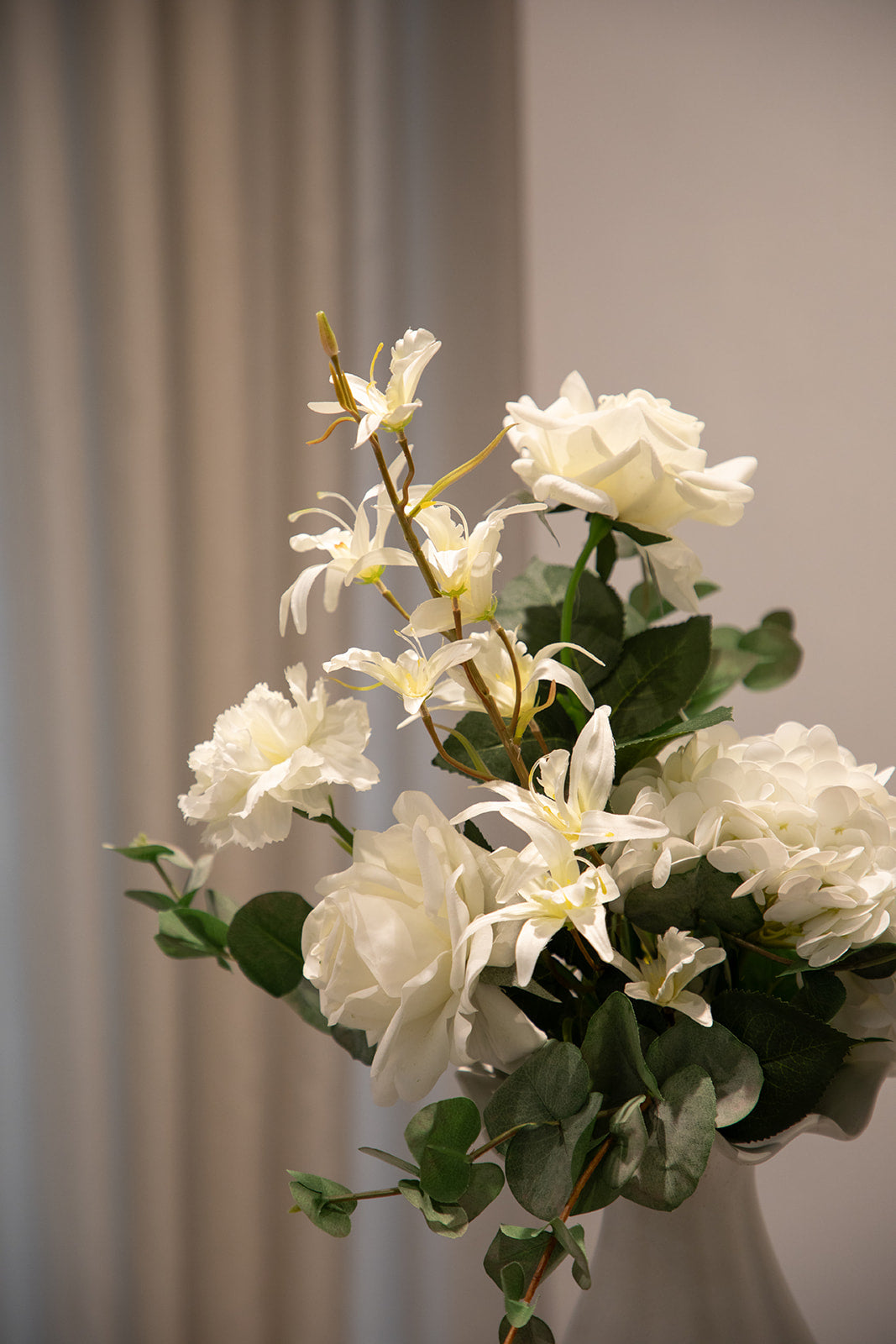 Nærbillede af buket af kunstige blomster i hvide og grønne nuancer. Placeret i en hvid keramik vase.