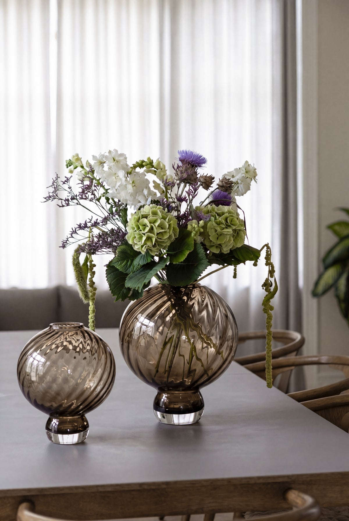 Stor Meadow glasvase i brun med drejende mønster, der står på et spisebord sammen med en mindre vase.