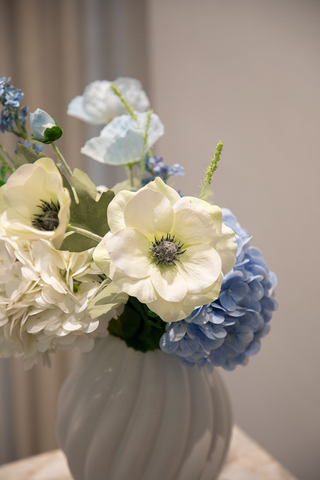 Nærbillede af buket af kunstige blomster i hvide og blå nuancer. Placeret i en hvid keramikvase