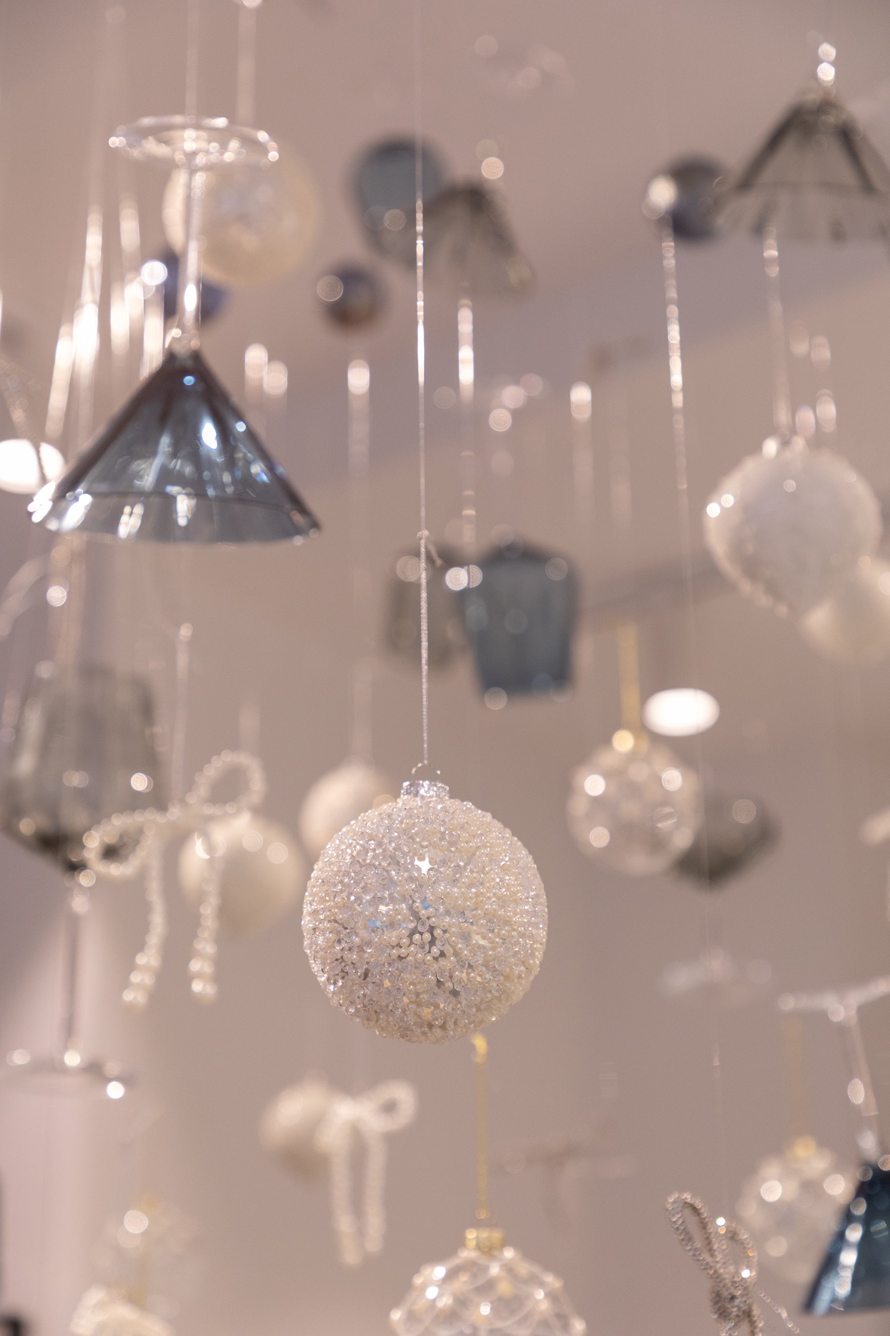 Billede af sølv julekugle med hvide perle detaljer, der hænger fra loftet blandt andre julekugler og glas.