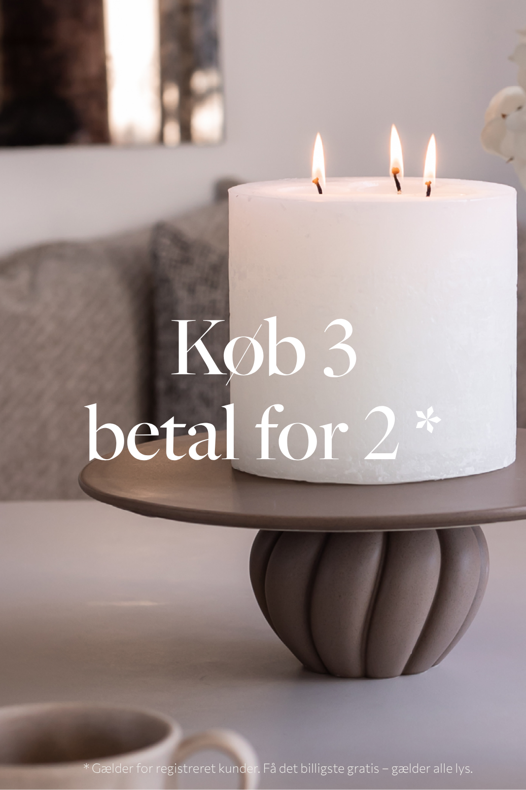 Et tændt tre-væddet hvidt bloklys placeret på et keramik kagefad. På billedet er teksten "køb 3 betal for 2" skrevet, dette gælder dog kun for registrerede kunder. Hvor man får det billigste gratis - gælder alle lys.