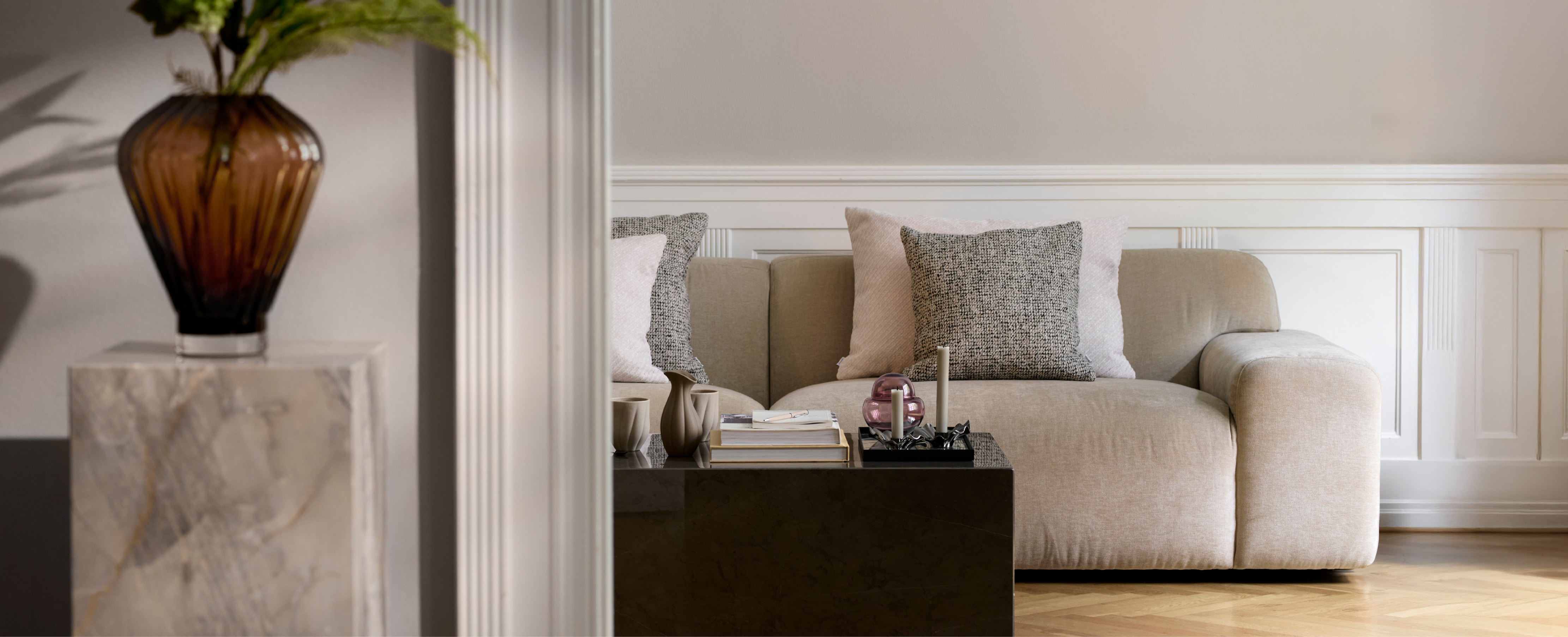 Beige sofa med hvide og grå puder. Foran er et marmor bord med service, lys og lysestager fra Specktrum