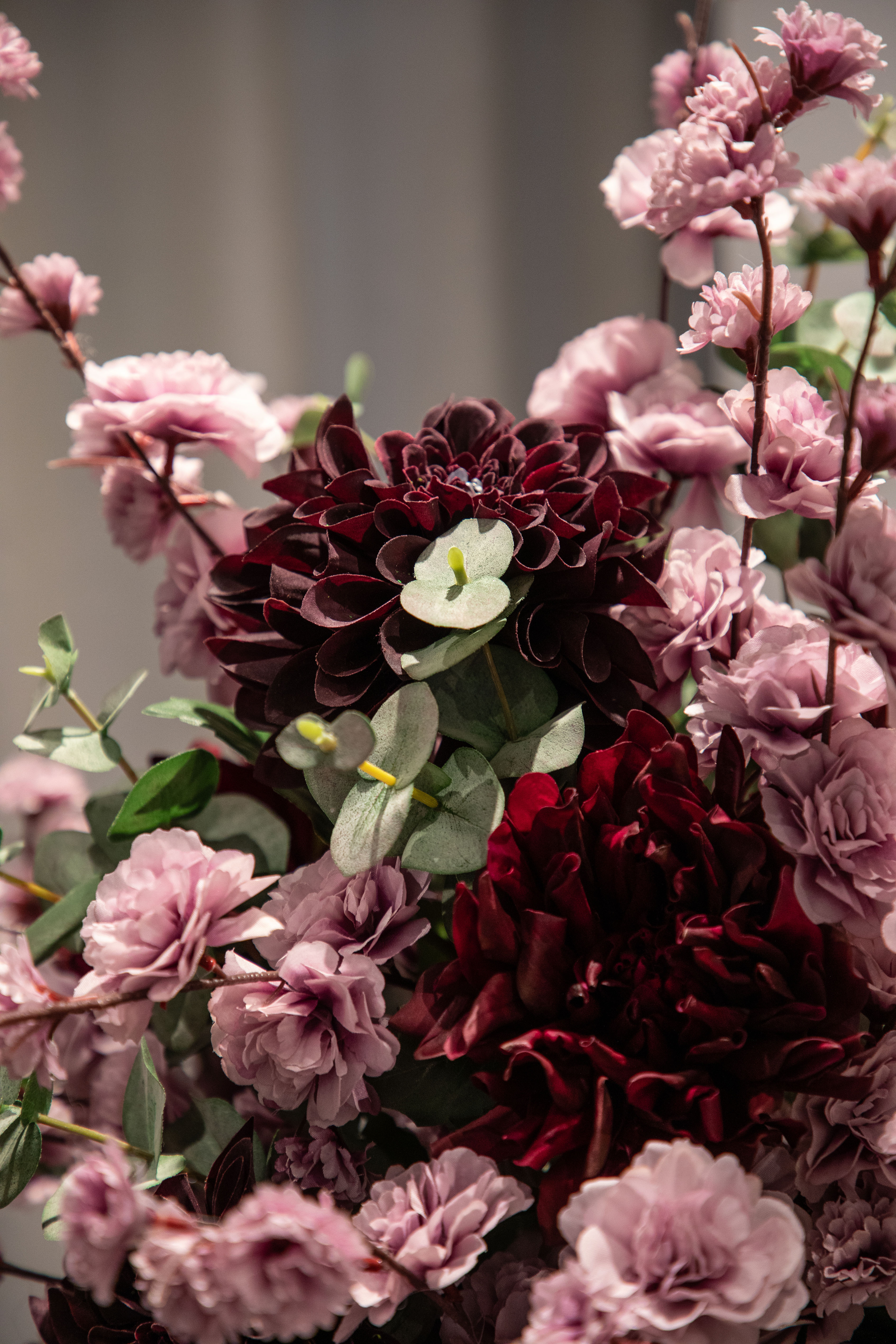 Nærbillede af stilke i rose, grønne og bordeaux nuancer, som er del af en større kunstig buket.