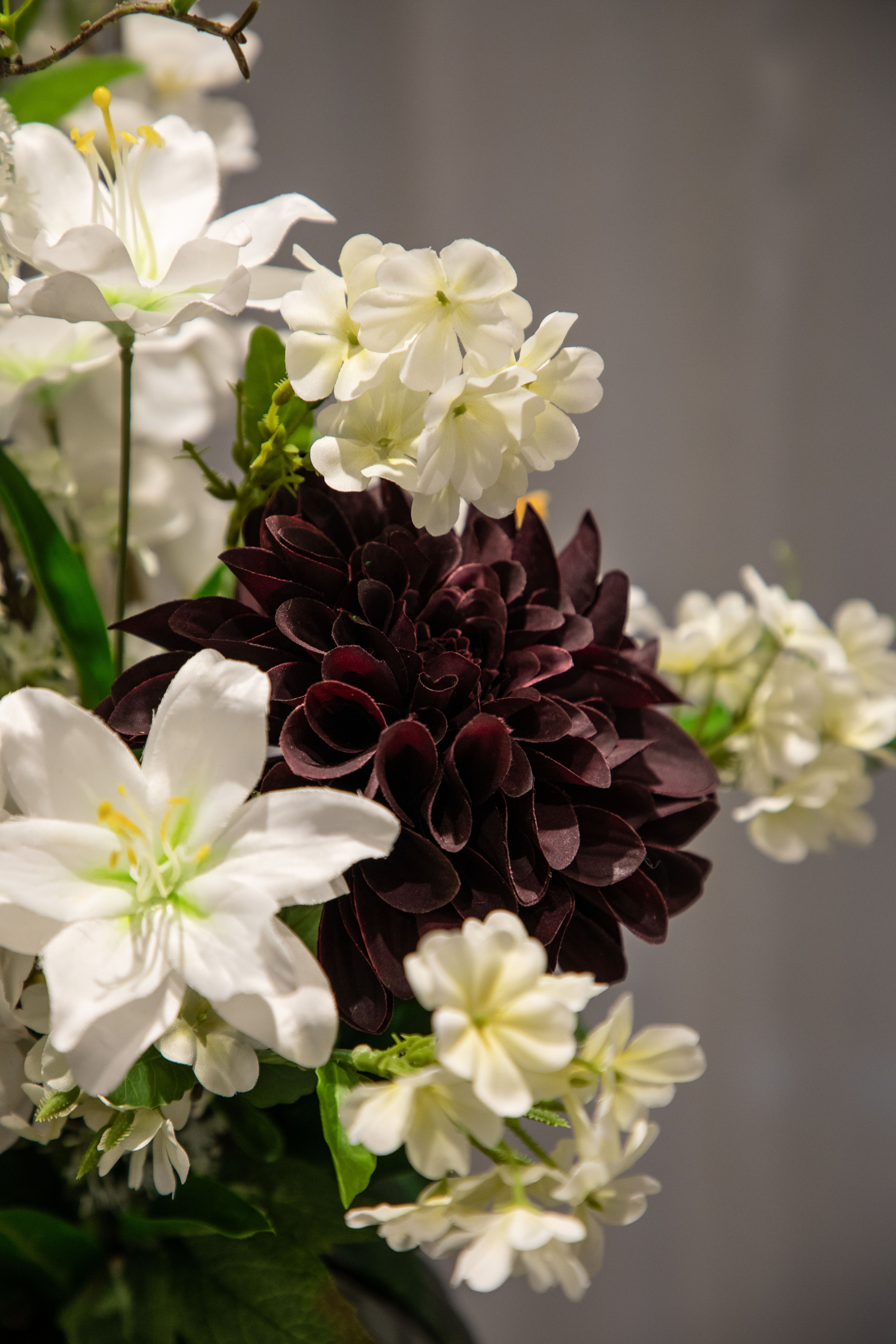 Nærbillede af bordeaux stilk, der er del af en større kunstig buket i hvide, grønne og røde nuancer.