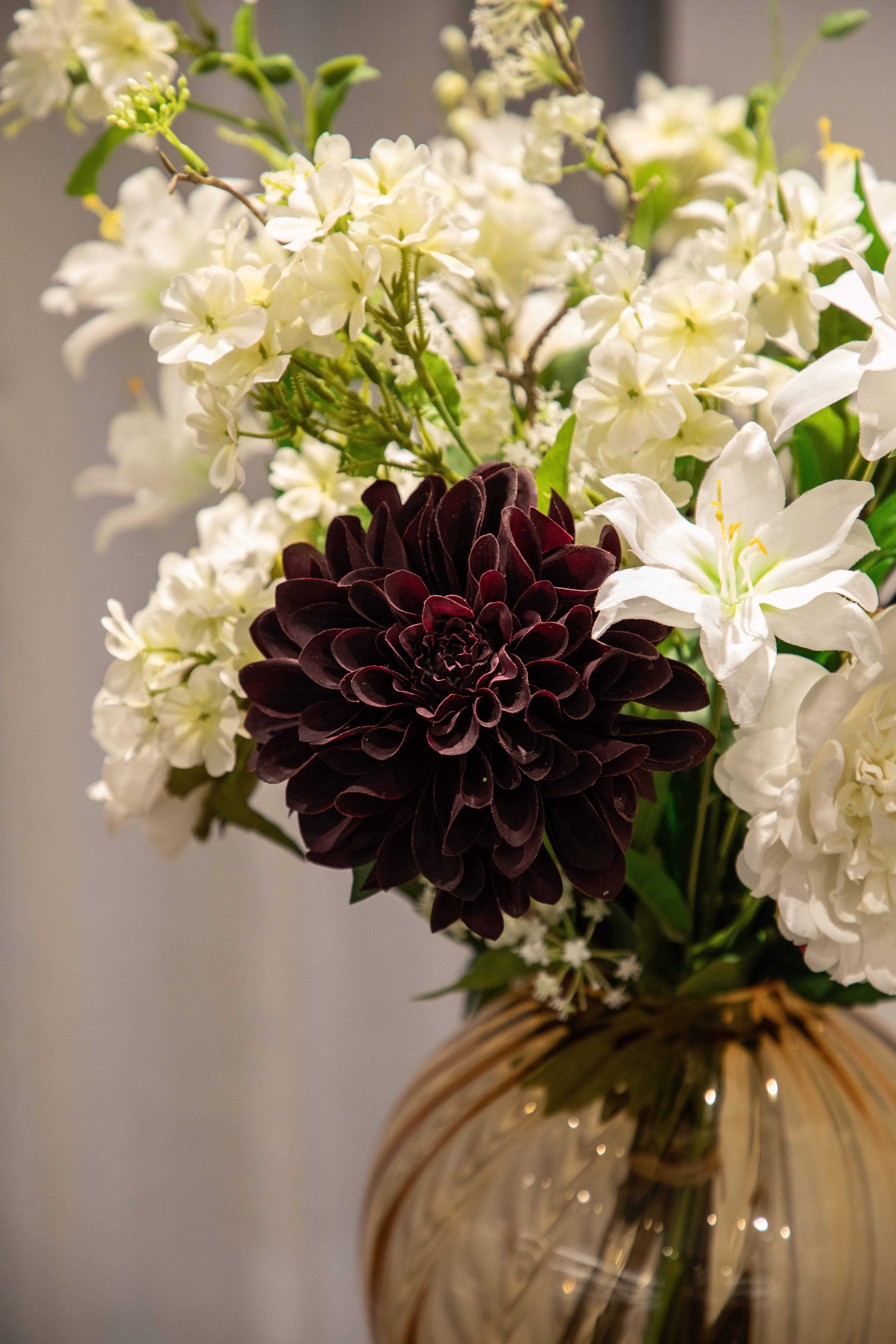 Nærbillede af kunstig buket i hvide, grønne og bordeaux nuancer, der står i en orange glas vase.