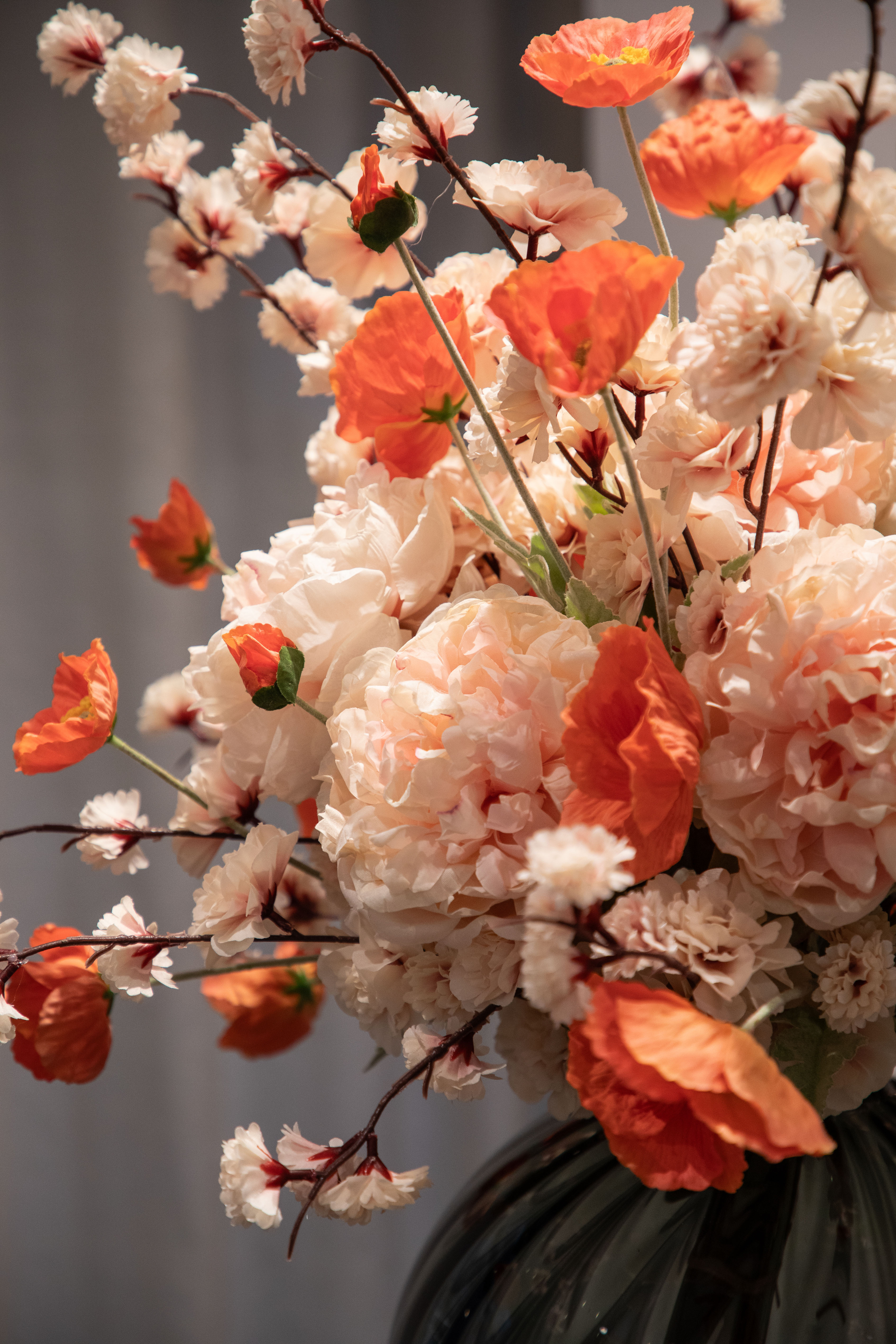 Nærbillede af en stor kunstig buket i sarte rose og orange nuancer, der er placeret i en grå rund glas vase.
