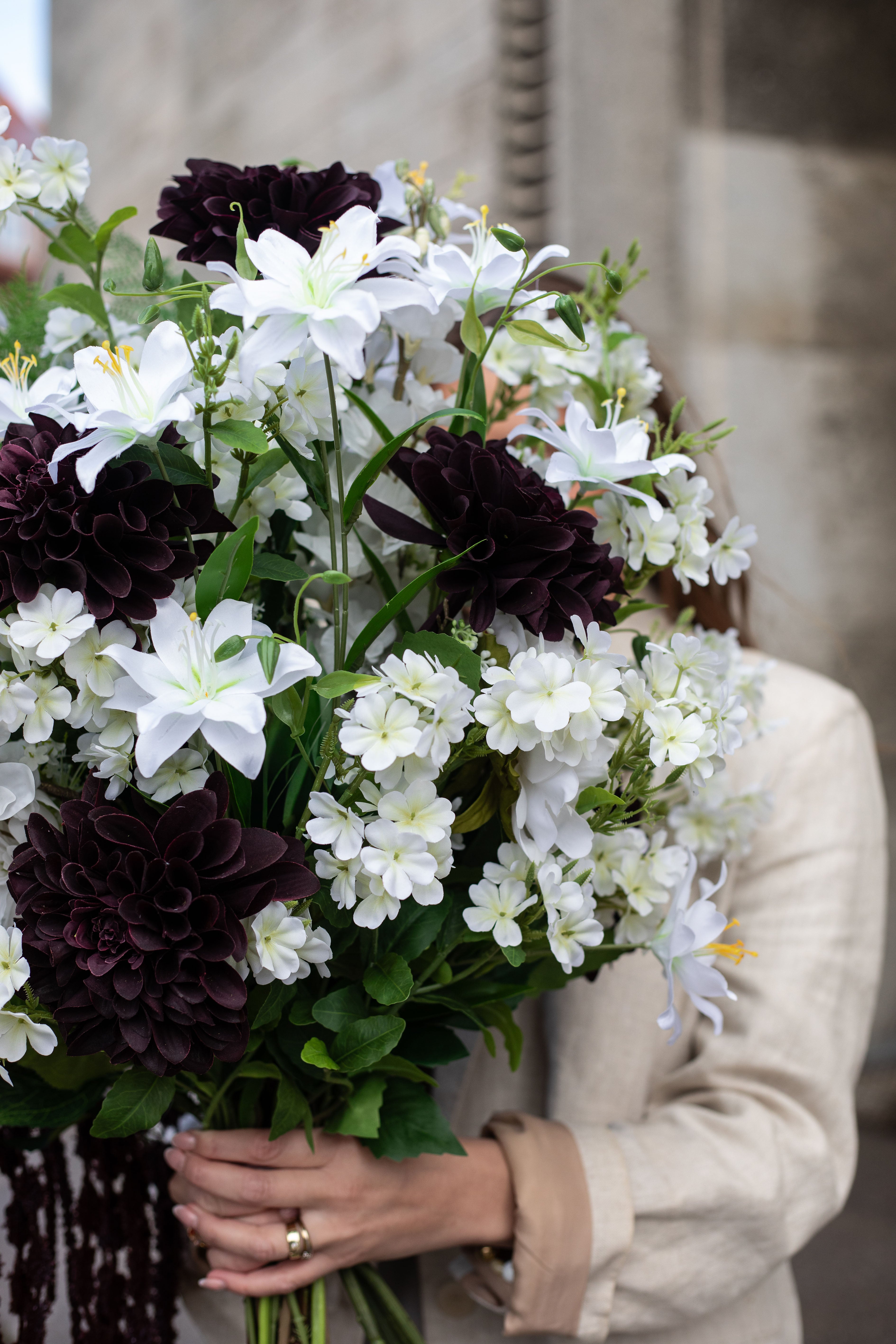 Nærbillede af en stor kunstig buket i hvide, grønne og bordeaux nuancer, der holdes af en pige op foran hovedet.