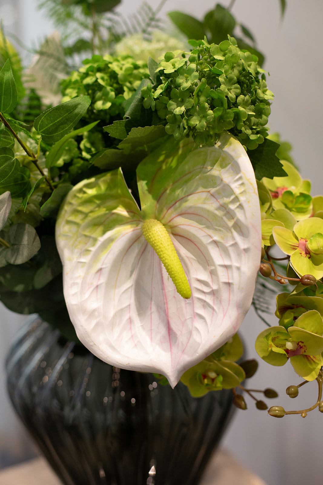 Nærbillede af kunstig buket, fokus er på en hvid flamingoblomst.