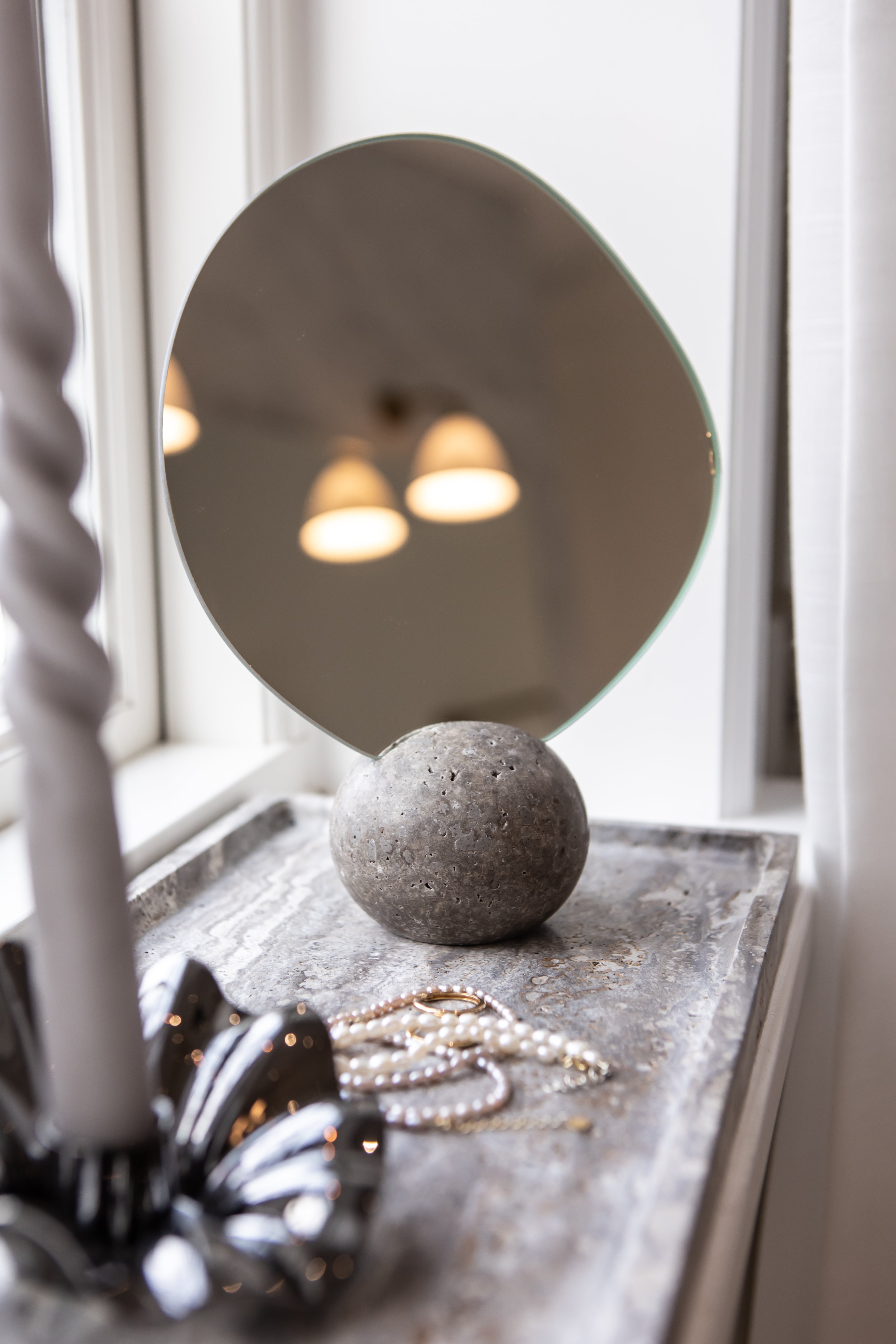 Asta bordspejlet med en travertin fod i farven thunderstorm stylet på en travertin bakke på et badeværelse.