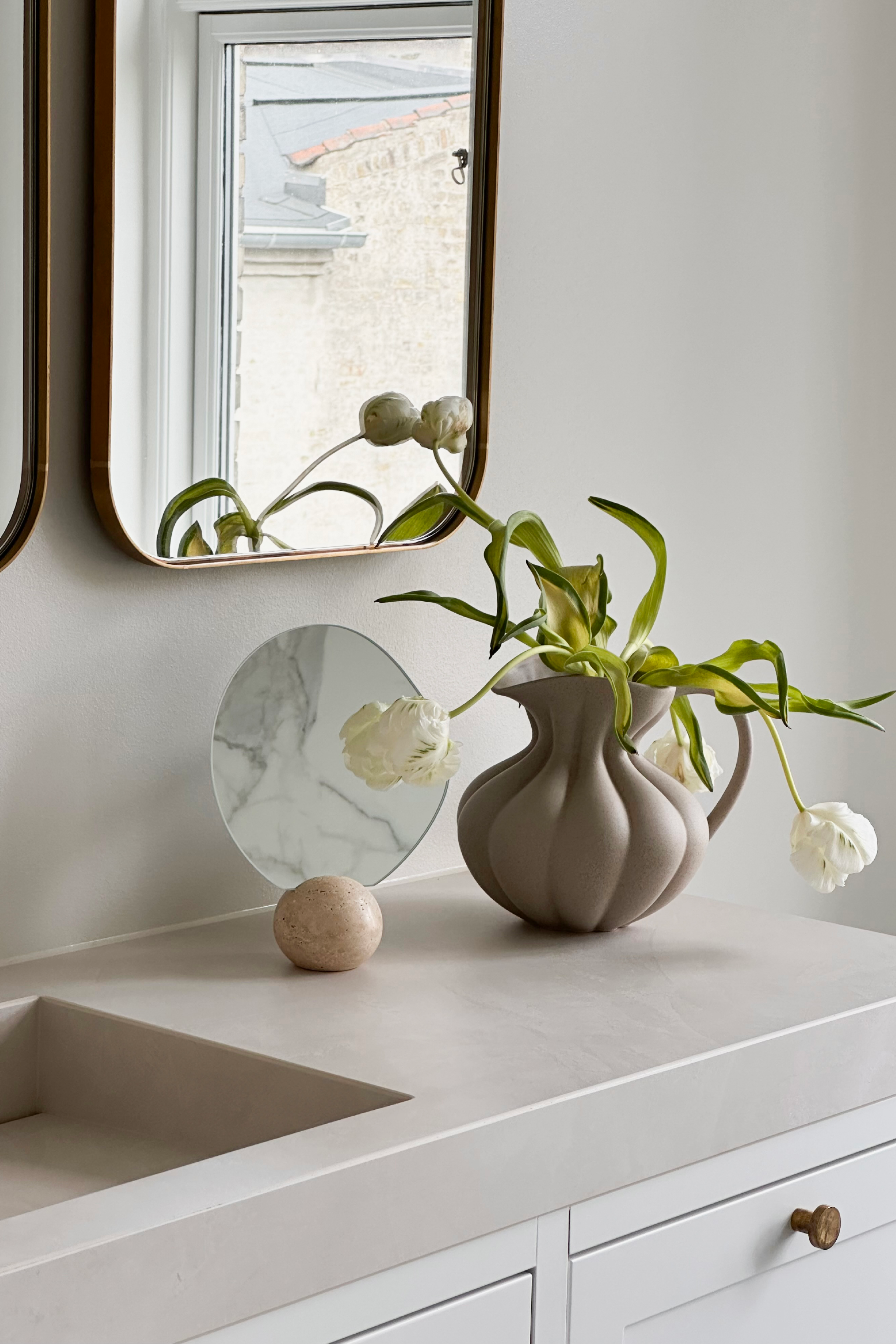 Asta bordspejlet stylet på et badeværelse ved siden af Nellie kanden med tulipaner i.