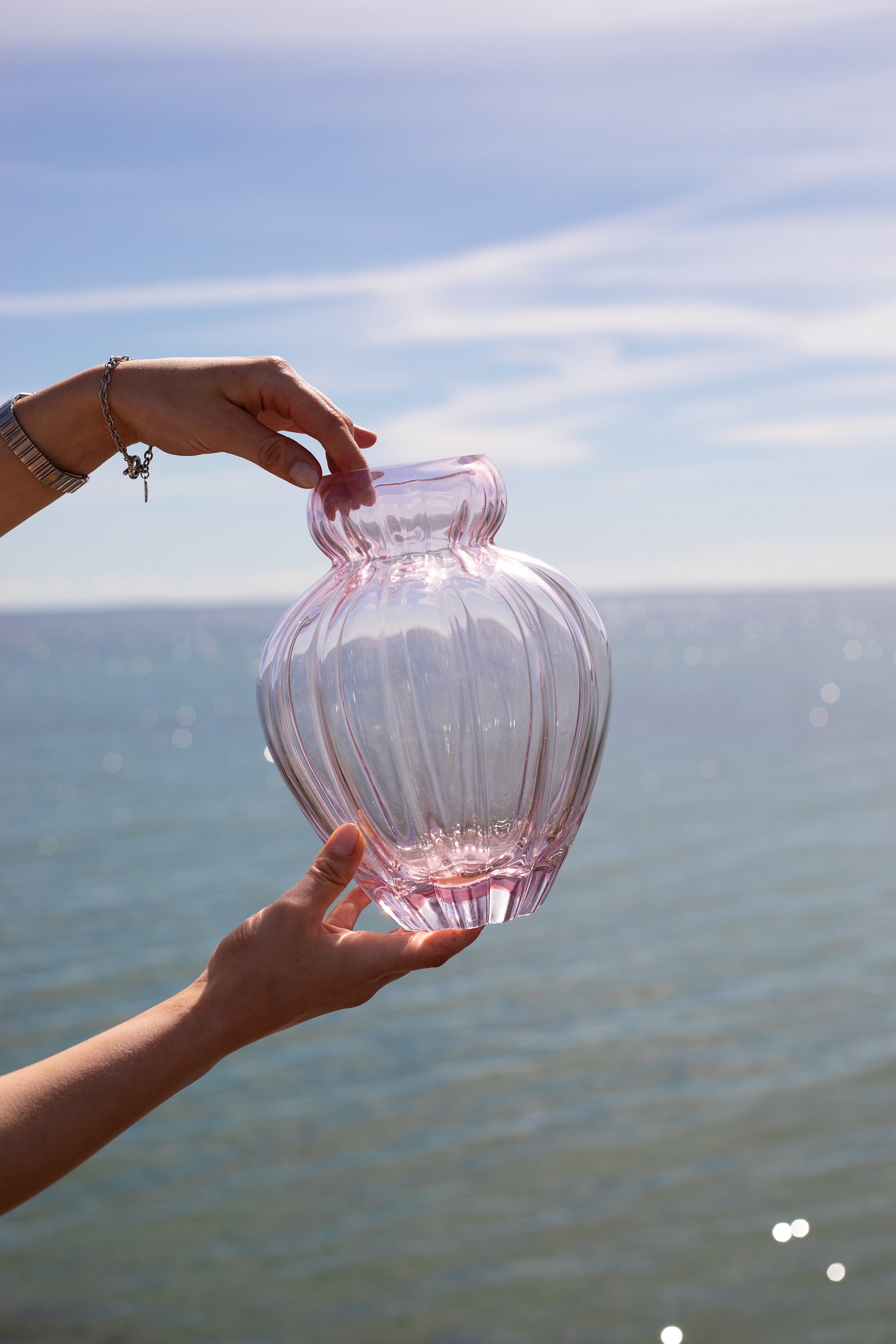 Audrey vasen i størrelse medium i rose, holdt op udover havet. Vasen er mundblæst i krystalglas.