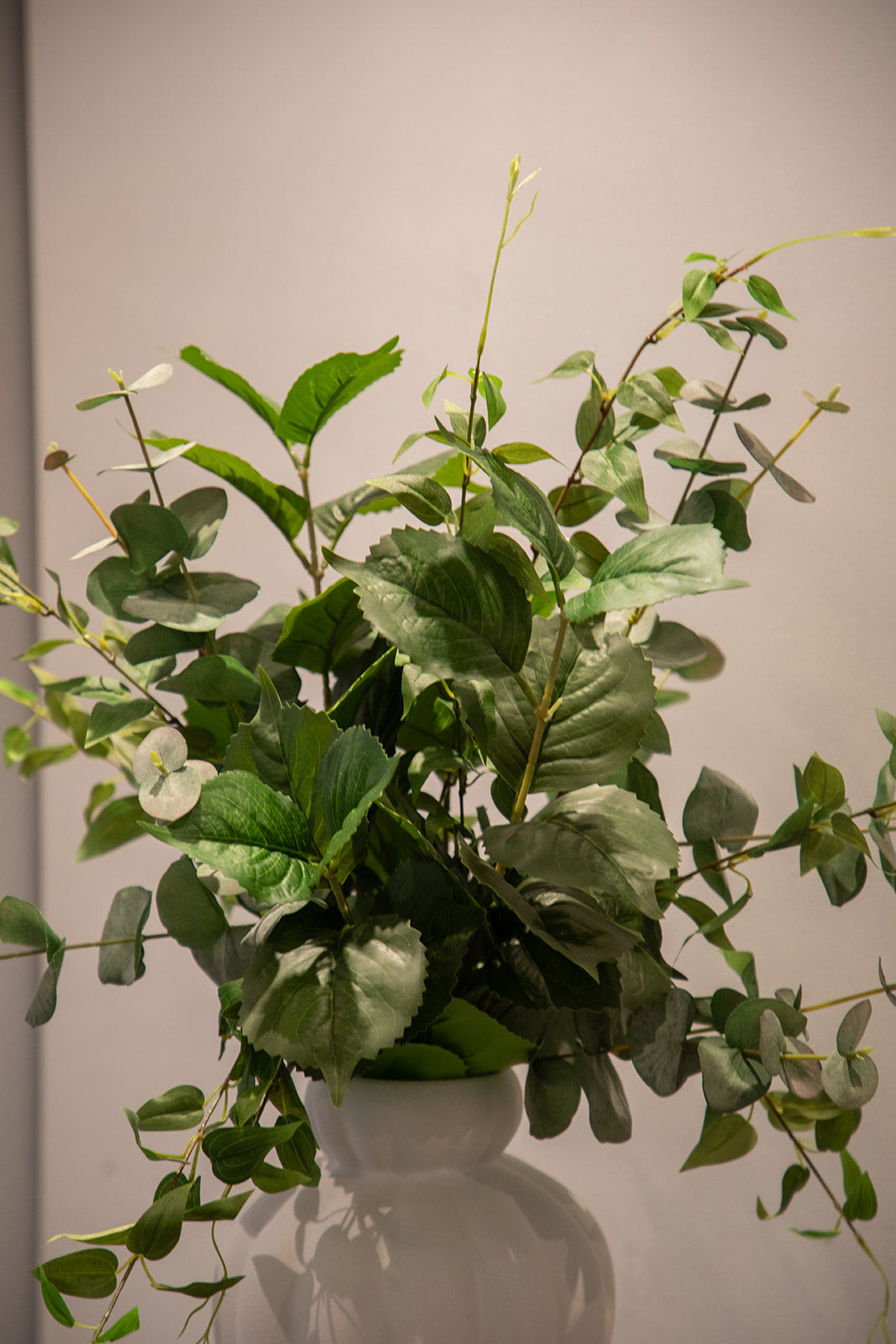 Nærbillede af kunstig blomster buket i grønne nuancer, der står i en hvid keramik vase.