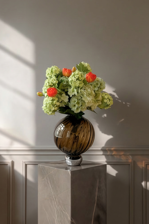 Grøn buket med rødorange tulipaner i en brun glasvase med swirlende mønster.