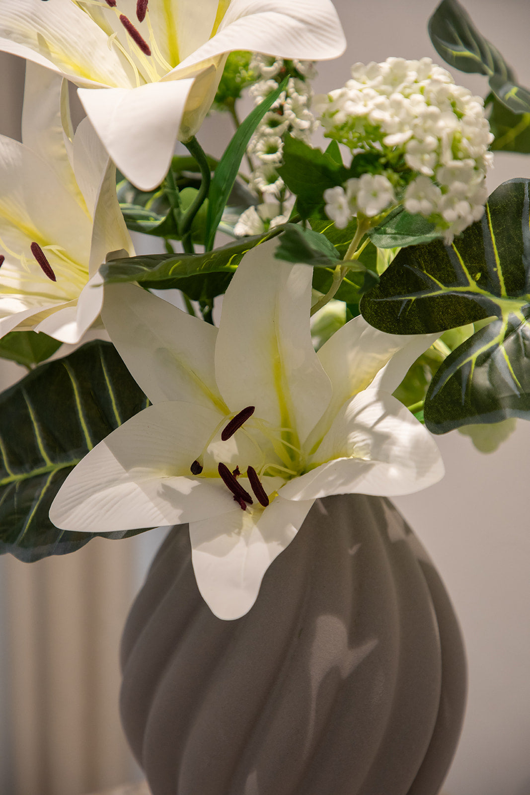 Nærbillede af buket af kunstige blomster i grønne og hvide nuancer. Placeret i en keramikvase.