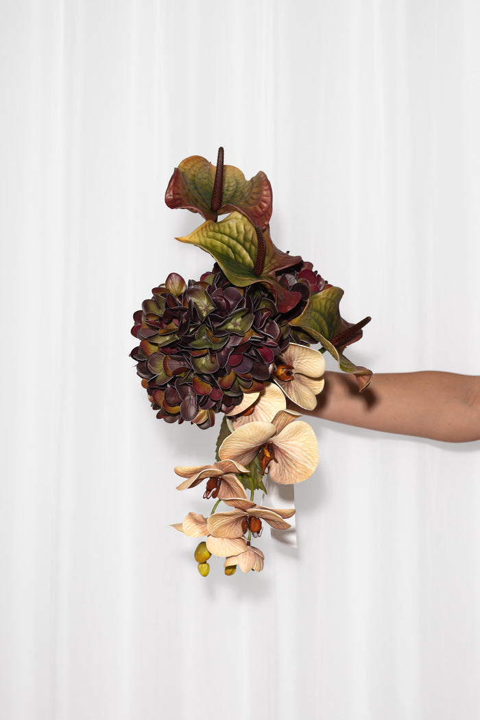 En betagende og skulpturel brudebuket i brændte rødlige, grønne og bordeaux nuancer. Brudebuketten består af en hortensia, orkide og flamigoblomster.