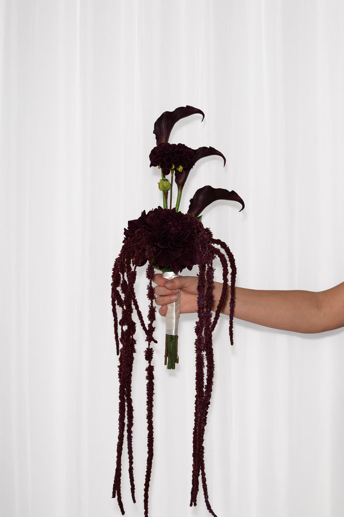 En skulpturel og dramatisk brudebuket i bordeaux farver. Brudebuketten er lavet af dahliaer, calla liljer og hængende blomster.
