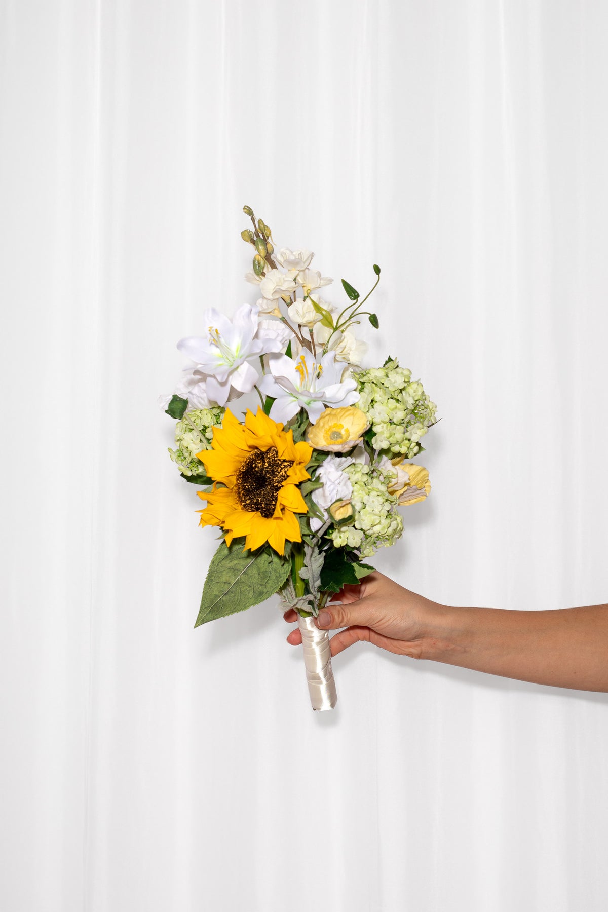 En sommerlig brudebuket af solsikker, valmuer og andre luftige blomster. Brudebuketten er i lyse farver som gul, hvid og lysegrøn. 