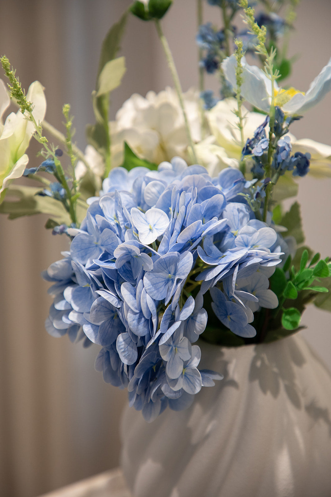 Nærbillede af blå hortensia, der er en del af en buket i blå og hvide nuancer. Placeret i en hvid keramikvase.