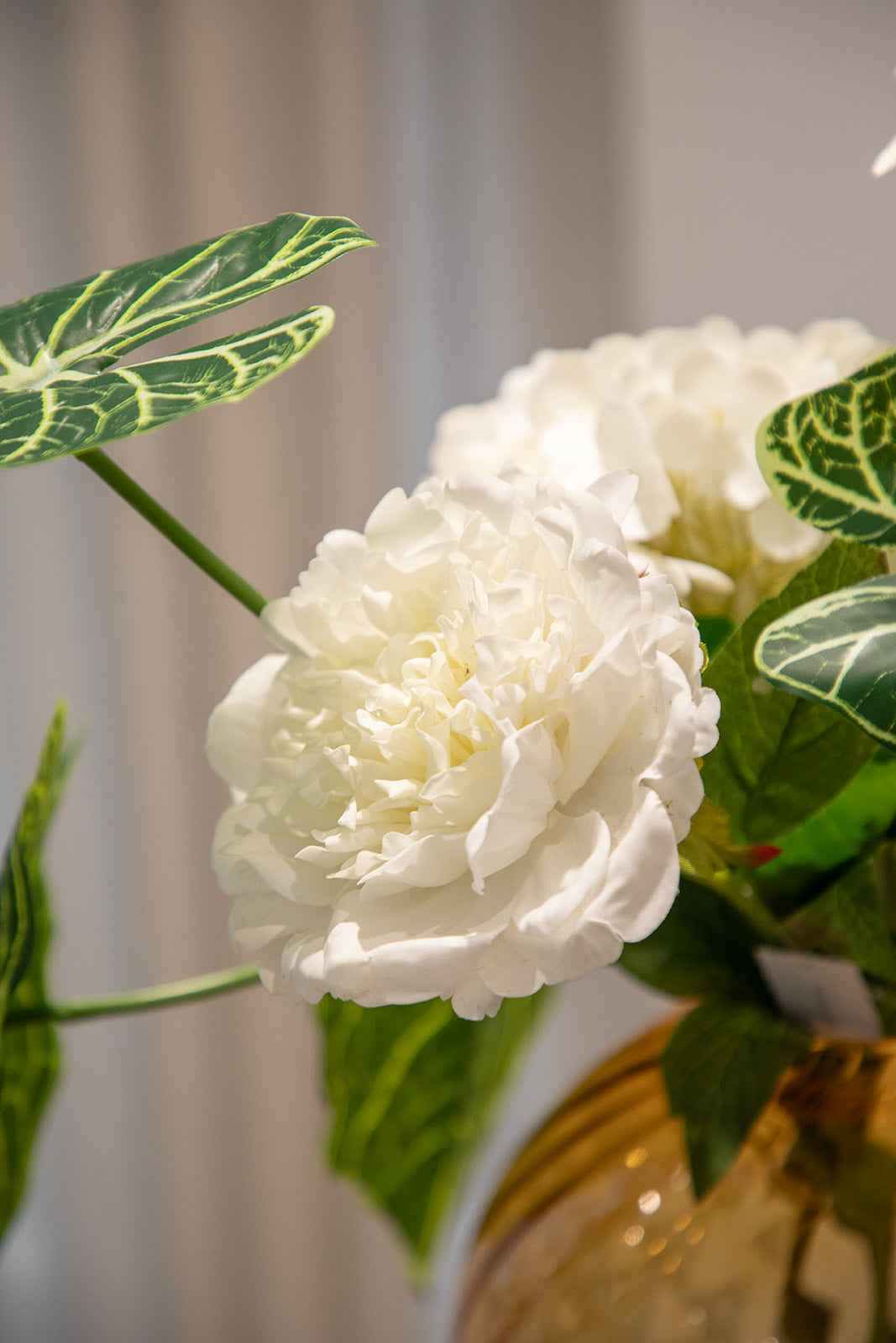 Nærbillede af buket i kunstige blomster i grønne og hvide nuancer. Placeret i en orange glasvase.