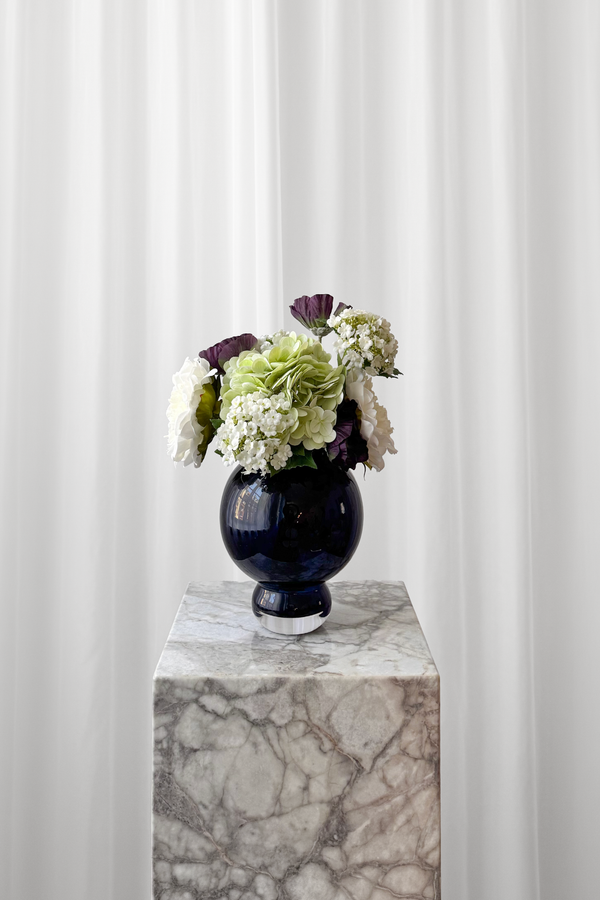 Lille buket i hvide, grønne og lilla nuancer stylet i en blå Meadow vase fra Specktrum.