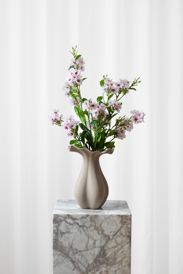 En lille til mellem størrelse buket af hvide og lyserøde kunstige blomster, som ser ægte ud. Buketten er stylet i en keramikvase.