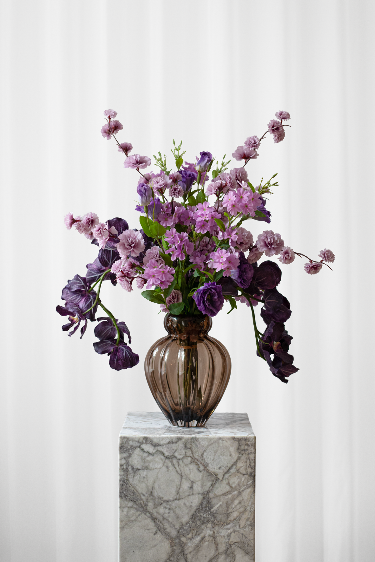 En mellem størrelse buket af kunstige, naturtro blomster i lilla farvenuancer.