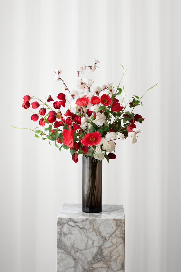 Luftig buket af røde og hvide blomster stylet i en brun glasvase.
