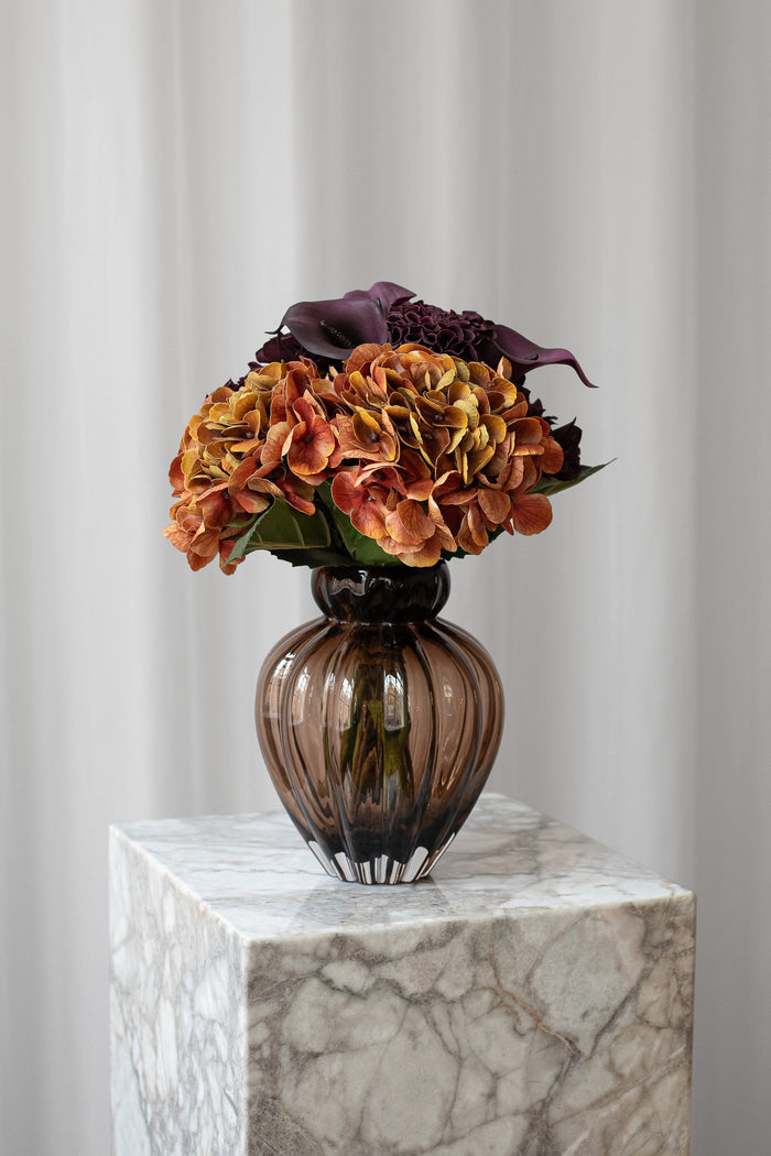 Buket Varm Poesi består af orange og mørkelilla / bordeaux blomster, såsom hortensia og calla liljer.