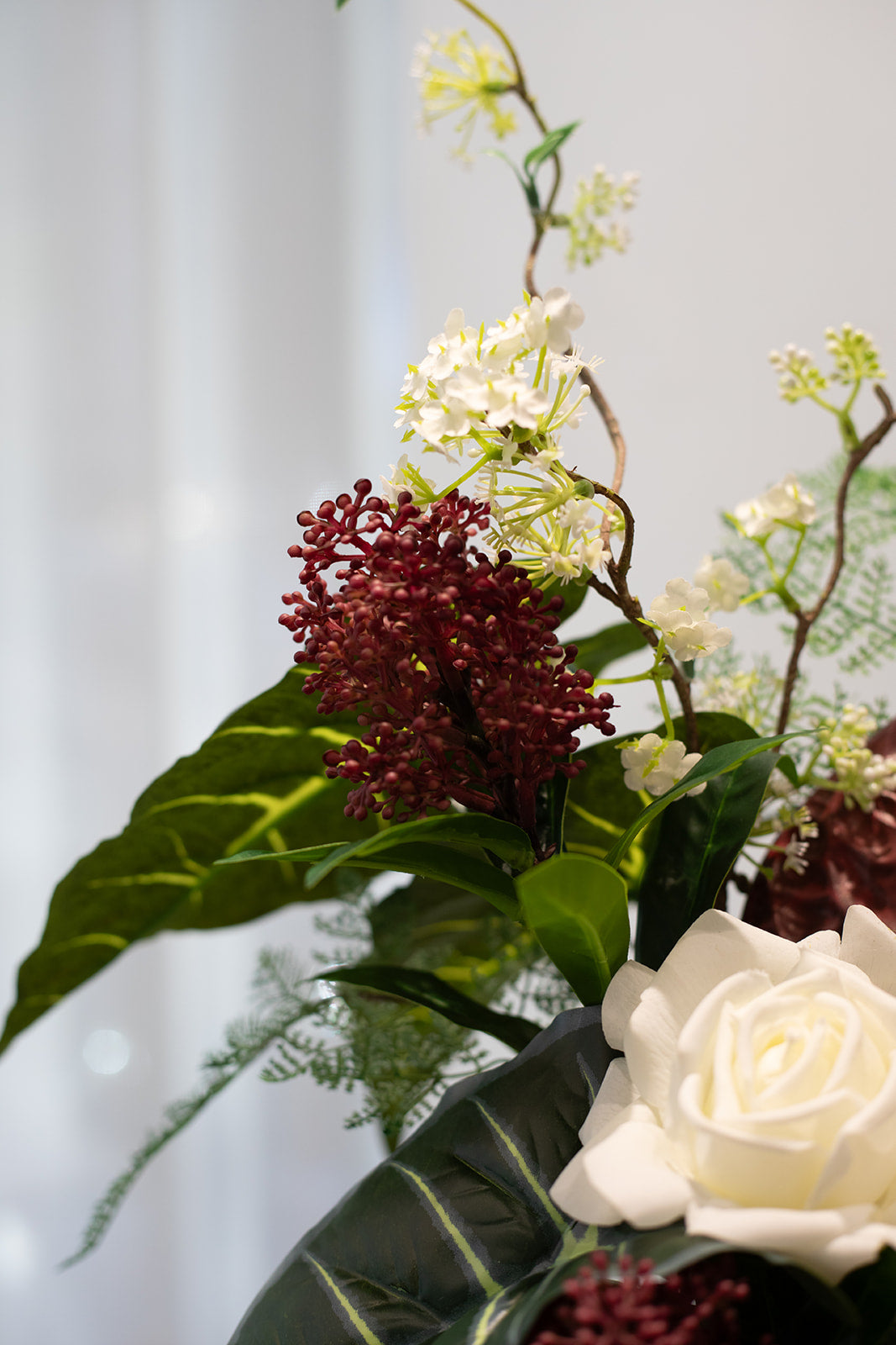 Nærbillede af få stilke fra en større kunstig buket i hvide, røde og grønne nuancer.