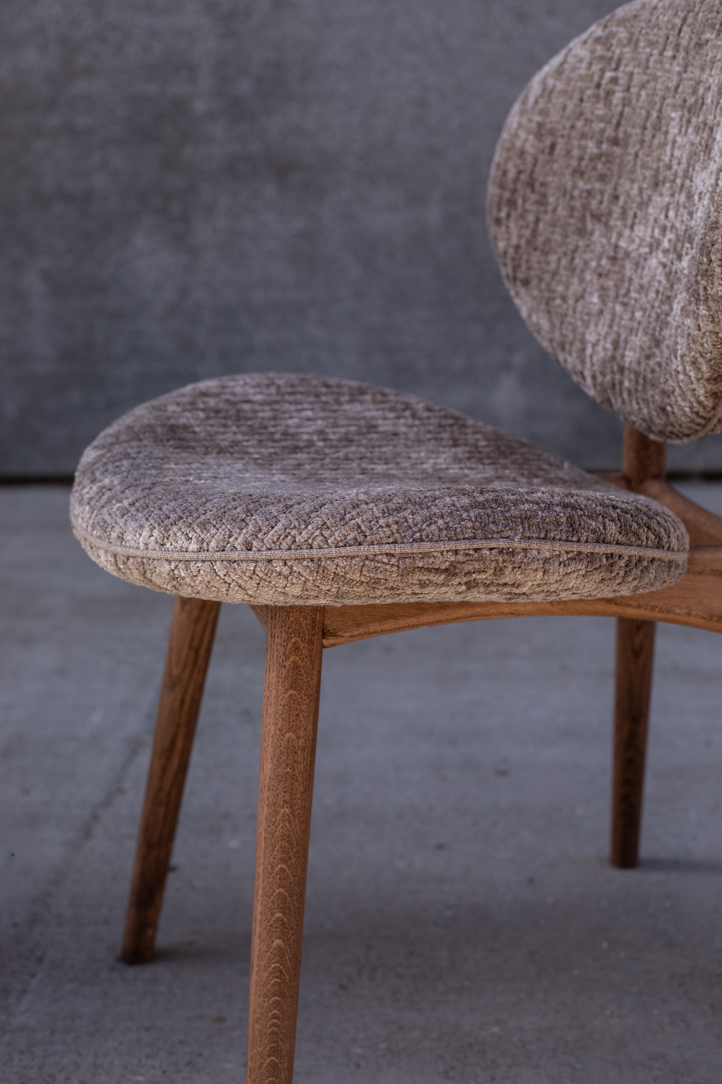 Detaljebillede af Nohr spisebordsstolen fra Specktrum. Stolen har et plysset, lysebrunt tekstil, en piping samt er lavet i FSC certificeret egetræ.