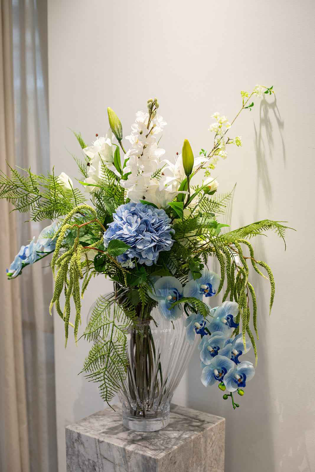 Stor buket i grønne, hvide og blå nuancer stylet i Evelyn vasen i stor klar.