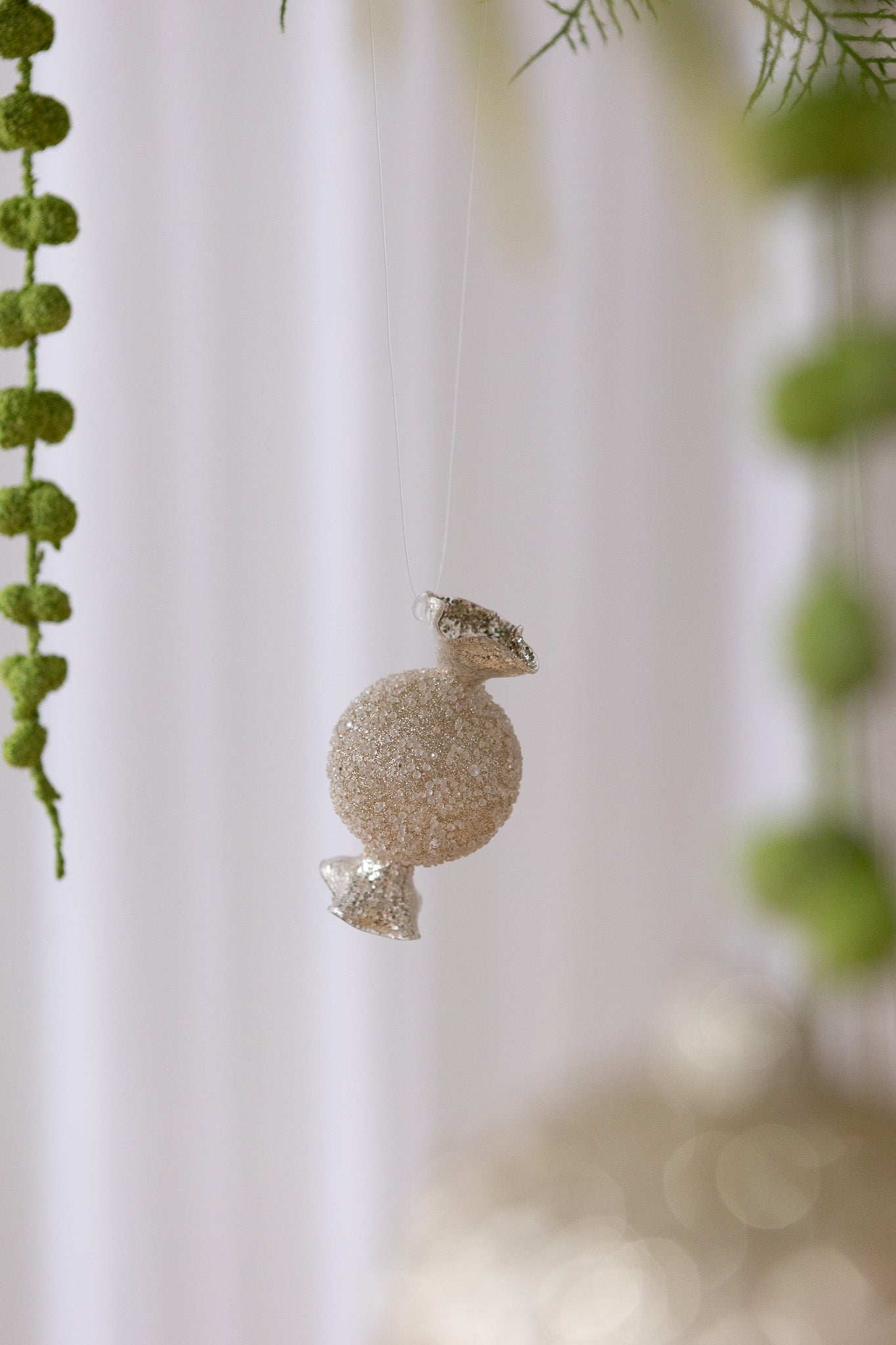 Nærbillede af Karamelformet julekugle i glas med guld glimmer og perler