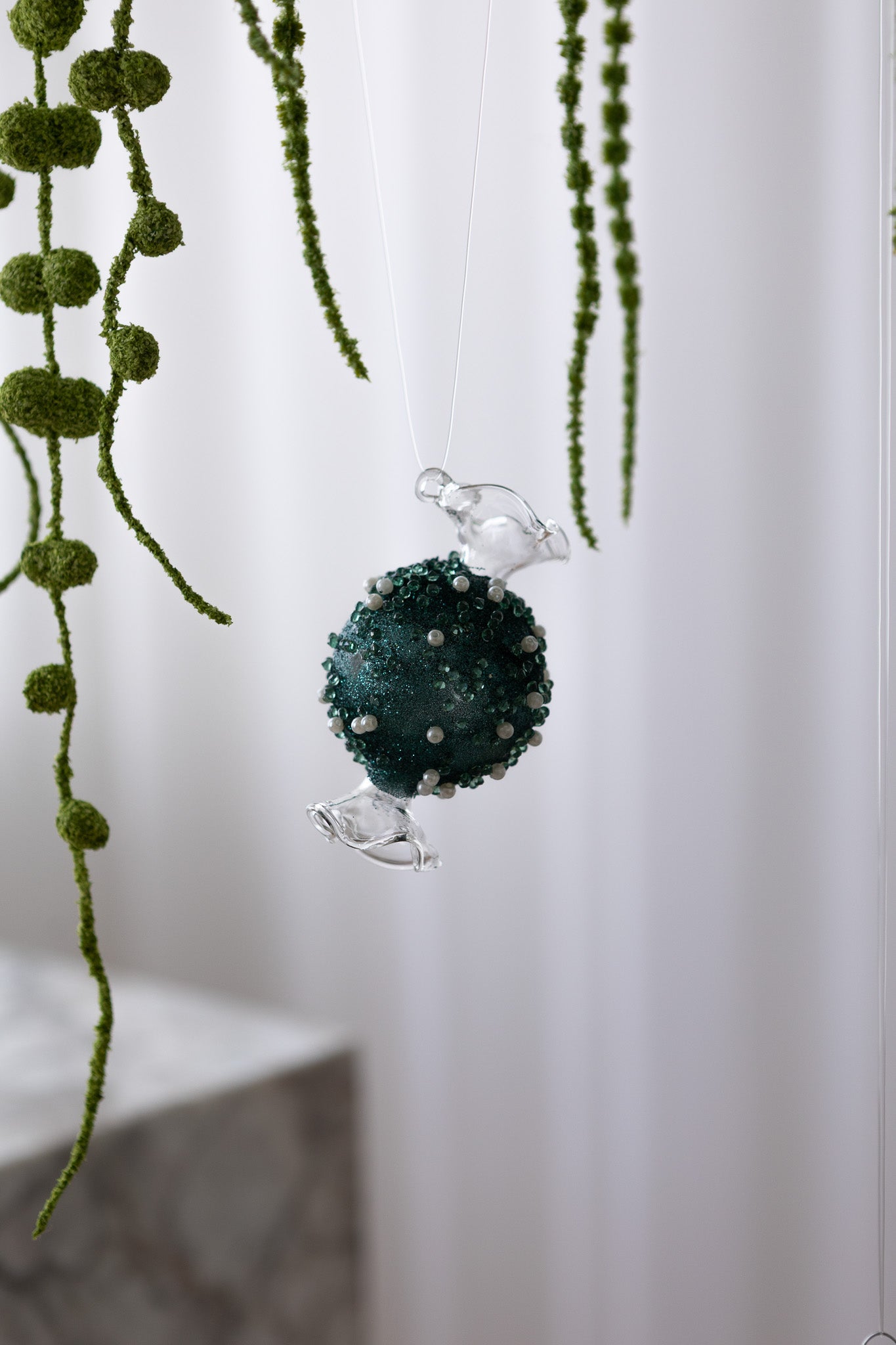 Nærbillede af Karamelformet julekugle i glas med grøn midte med glimmer og perler 