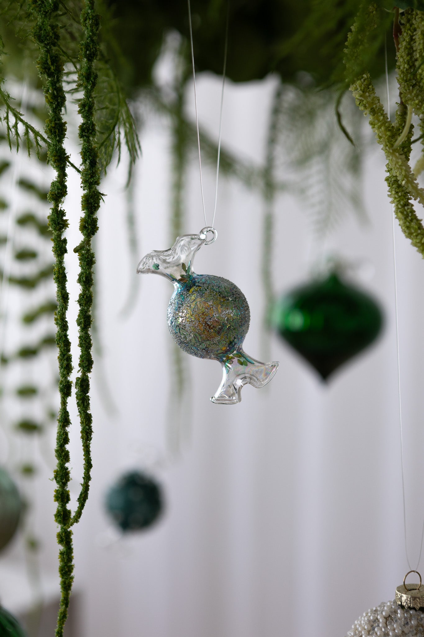 Nærbillede af Karamelformet julekugle i glas med grøn/multifarvet glimmermidte