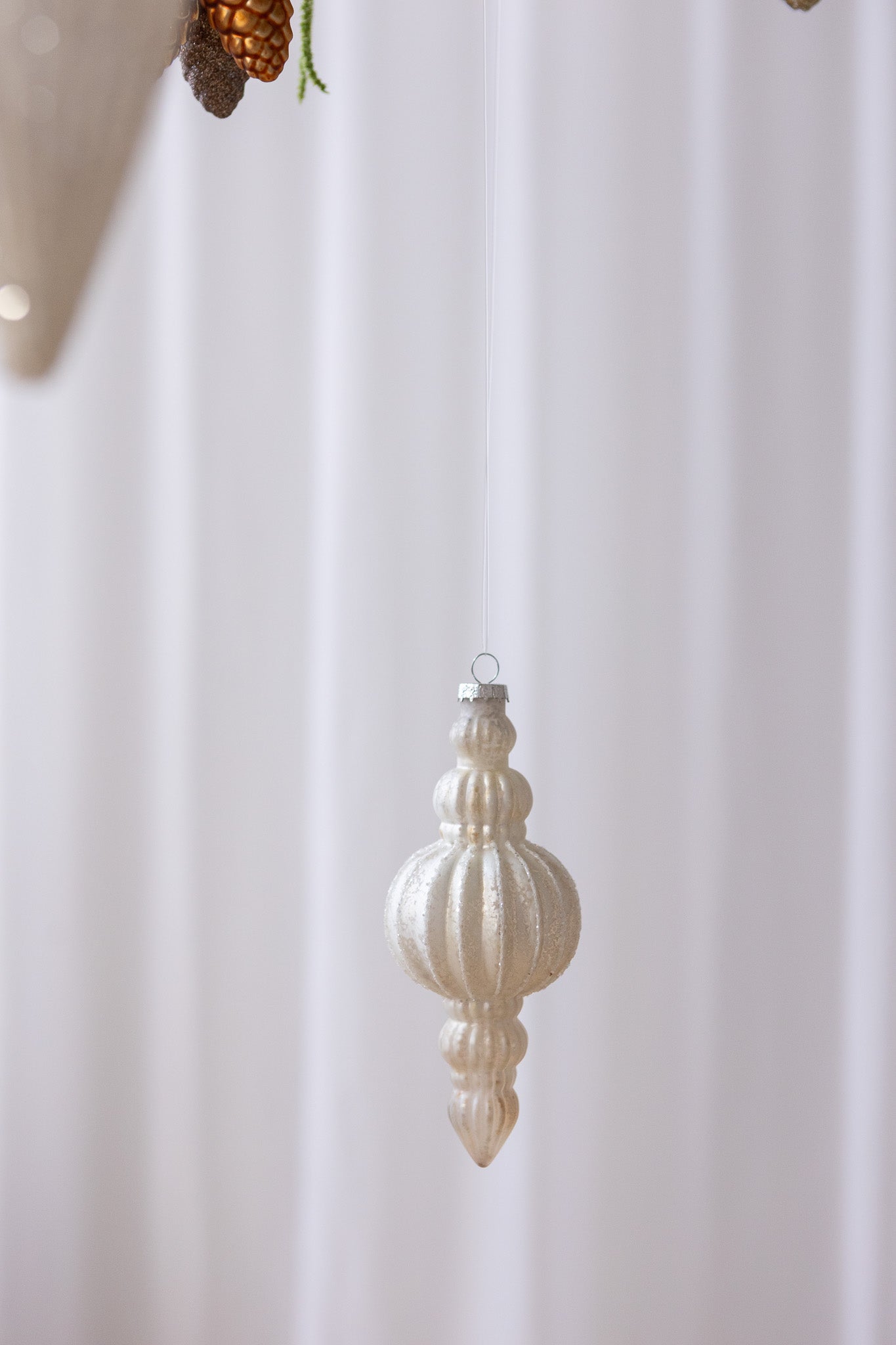 Nærbillede af Aflang julekugle med runde former i beige antik og med hvid glimmer