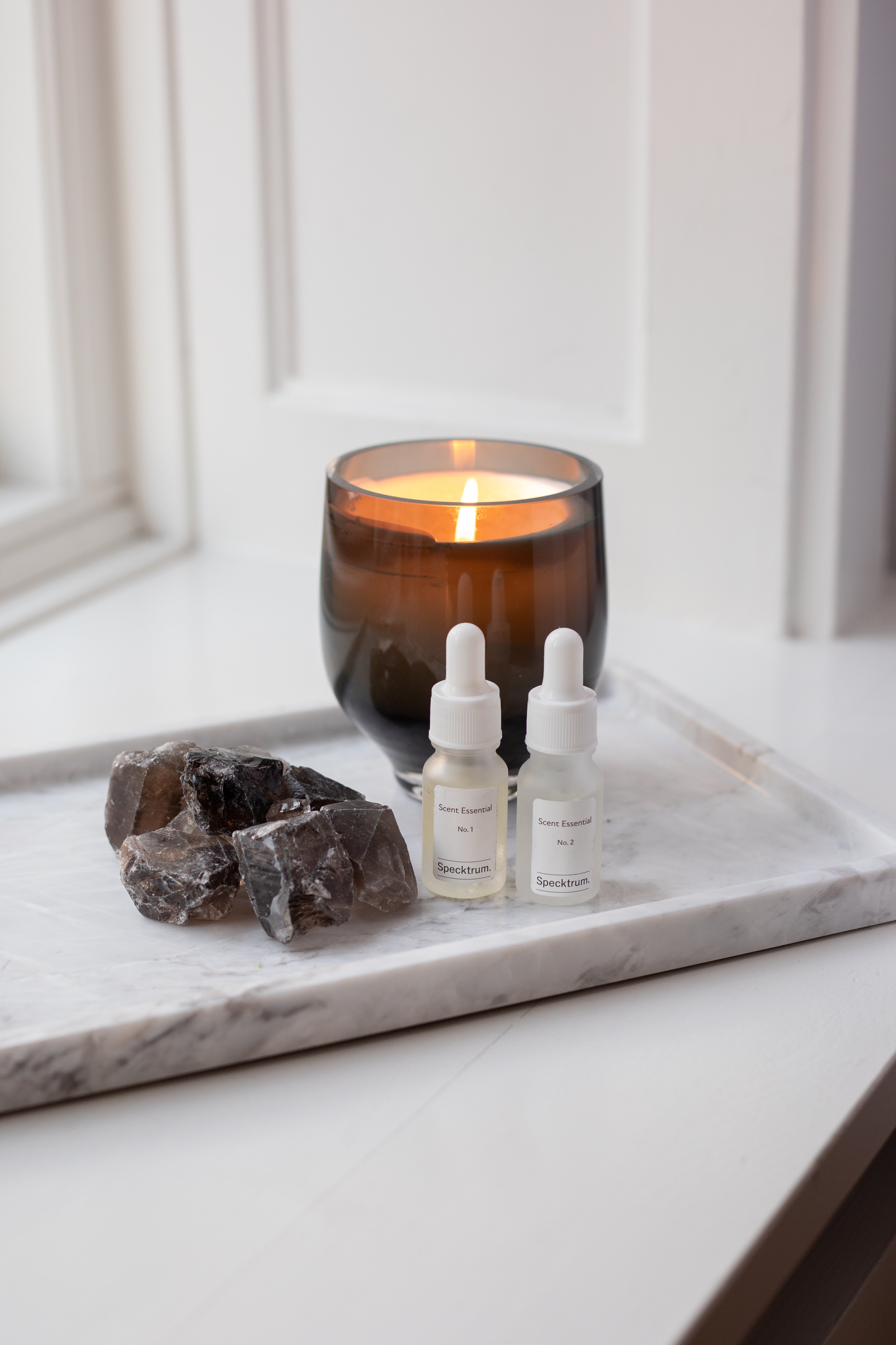Krystalsten i røgkvarts der ligger på en marmorbakke ved siden af et duftlys i farven amber og Specktrums Scent.