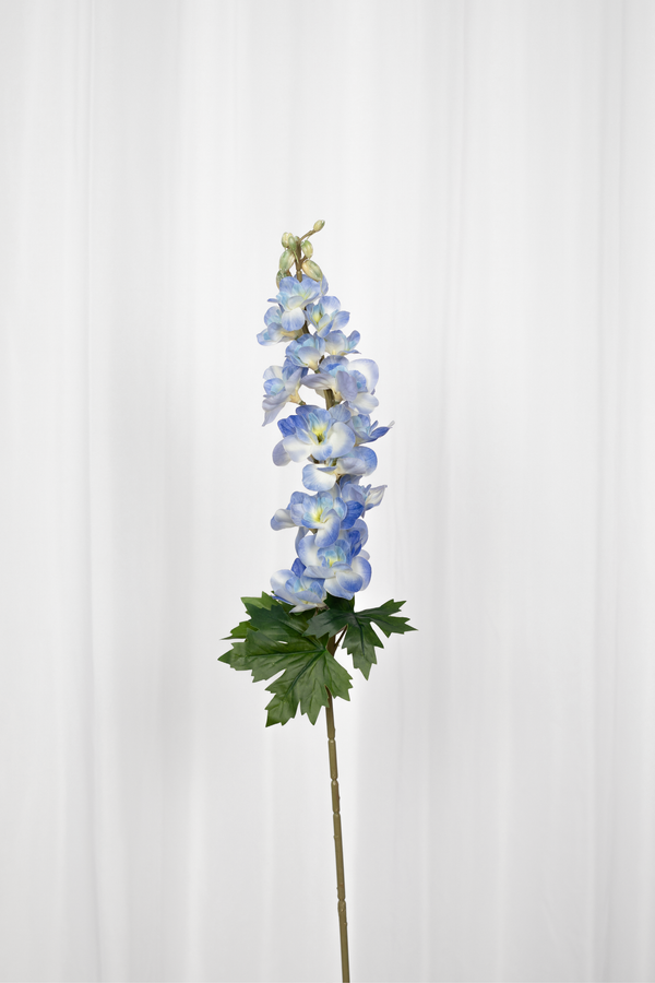Kunstig consolida blomst i blå med grønne blade i bunden. 
