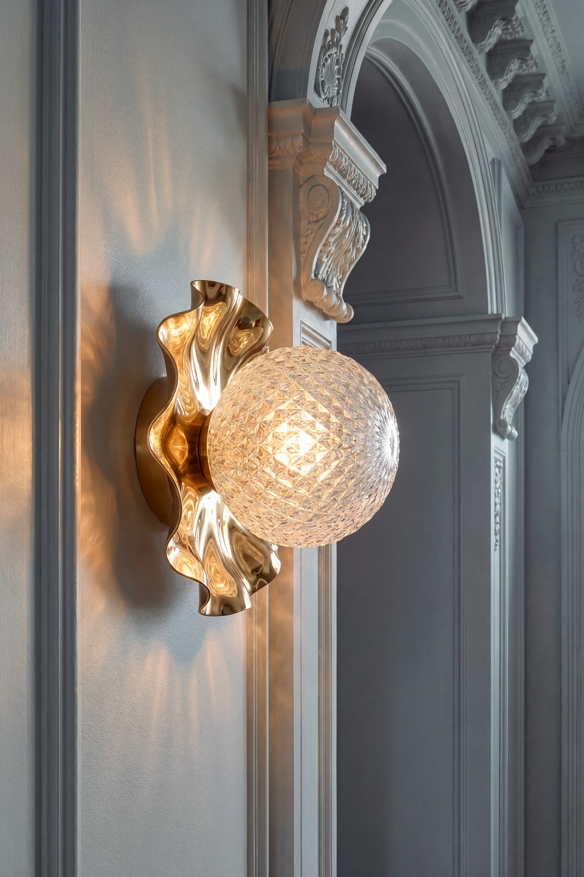 Lea lampen, der hænger i en gang. Lampens bløde, organiske former er i guld metal og glaskuglen er i klart glas med harlequin mønster.