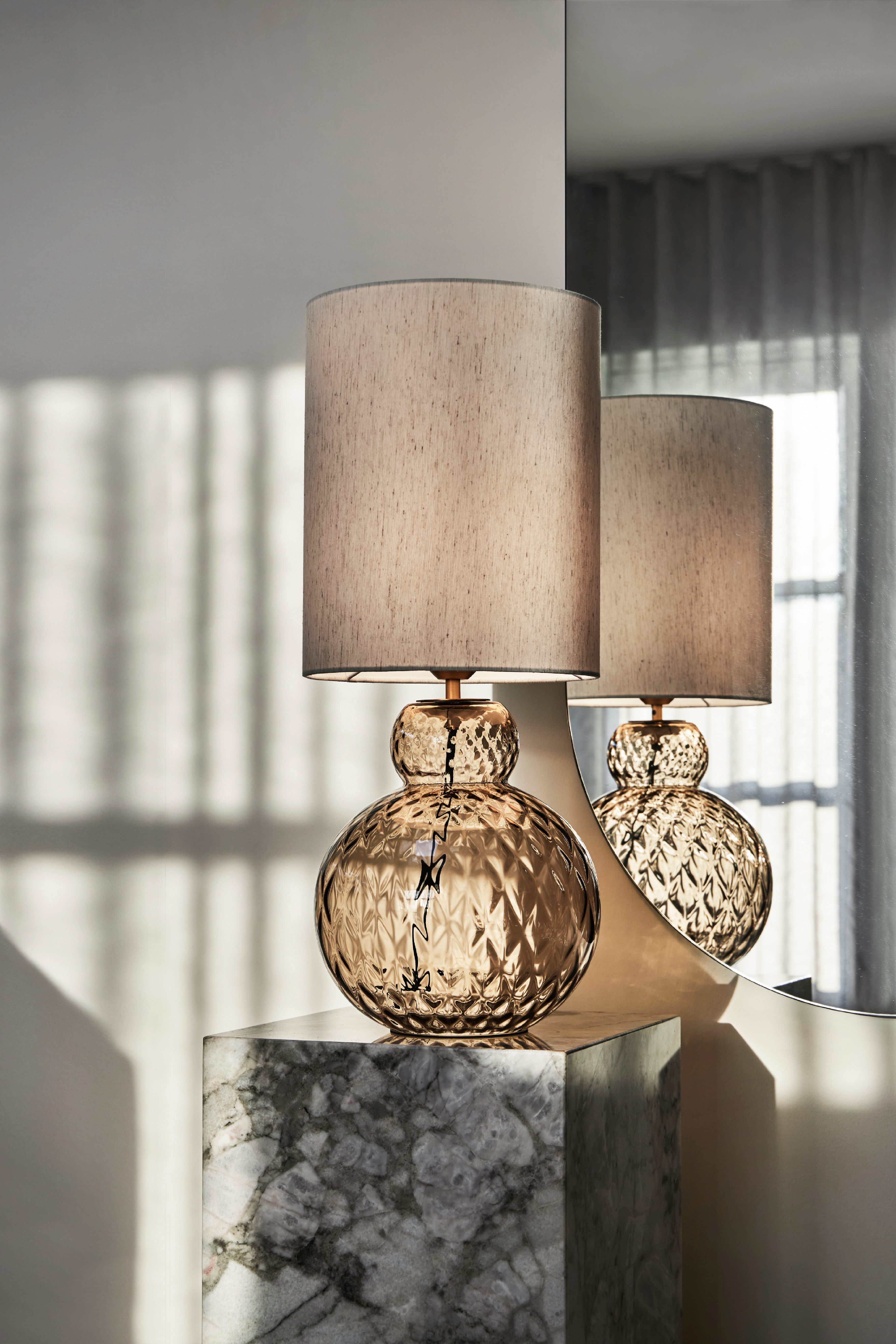 Lily bordlampe i brun med harlequin mønster med en høj lampeskærm. Lampen står på en marmor pedestal.