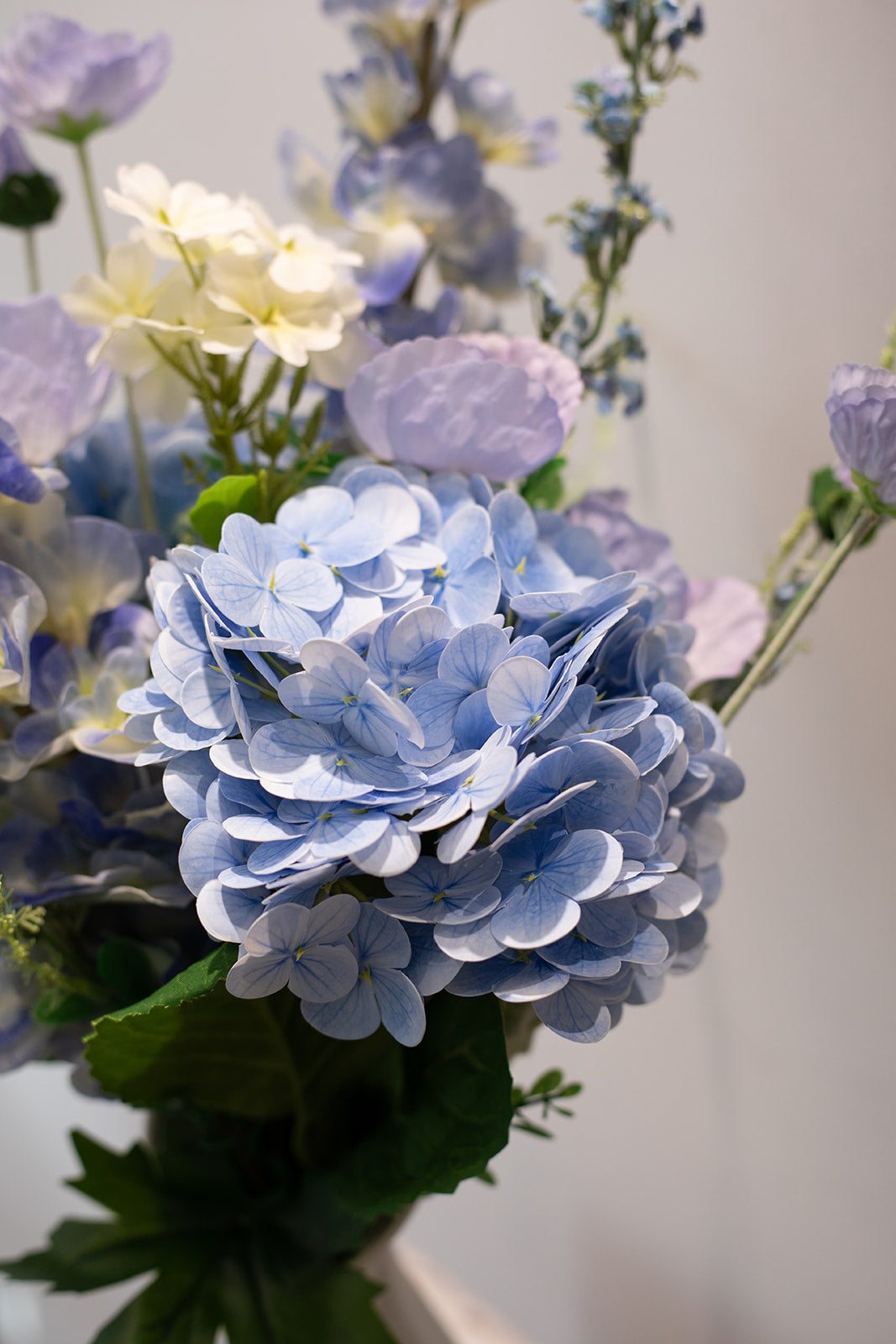 Nærbillede af kunstige stilke i blå, lilla, hvide og grønne nuancer, der er del af en større buket.