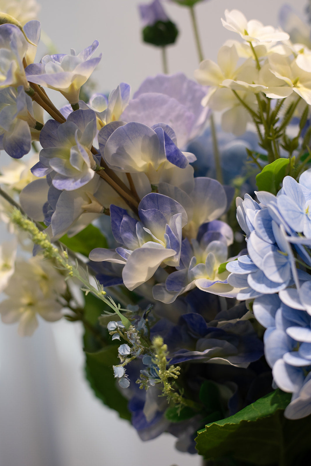 Nærbillede af kunstige stilke i blå, lilla, hvide og grønne nuancer, der er del af en større buket.