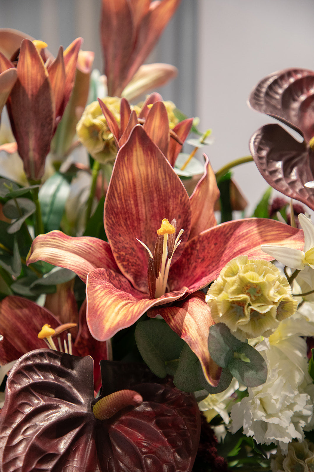 Nærbillede af en rød lilje, der er en del af en buket af kunstige blomster i røde, hvide og creme farver.