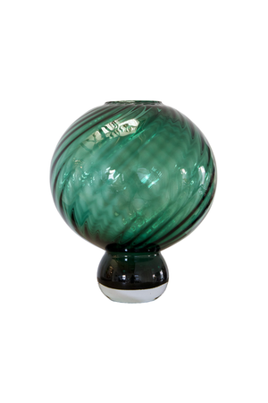 En rund, mundblæst glasvase i en dyb grøn farve med dekorative spiralformede mønstre, der snor sig rundt om formen. Vasen står på en lille, mørkere glasfod.