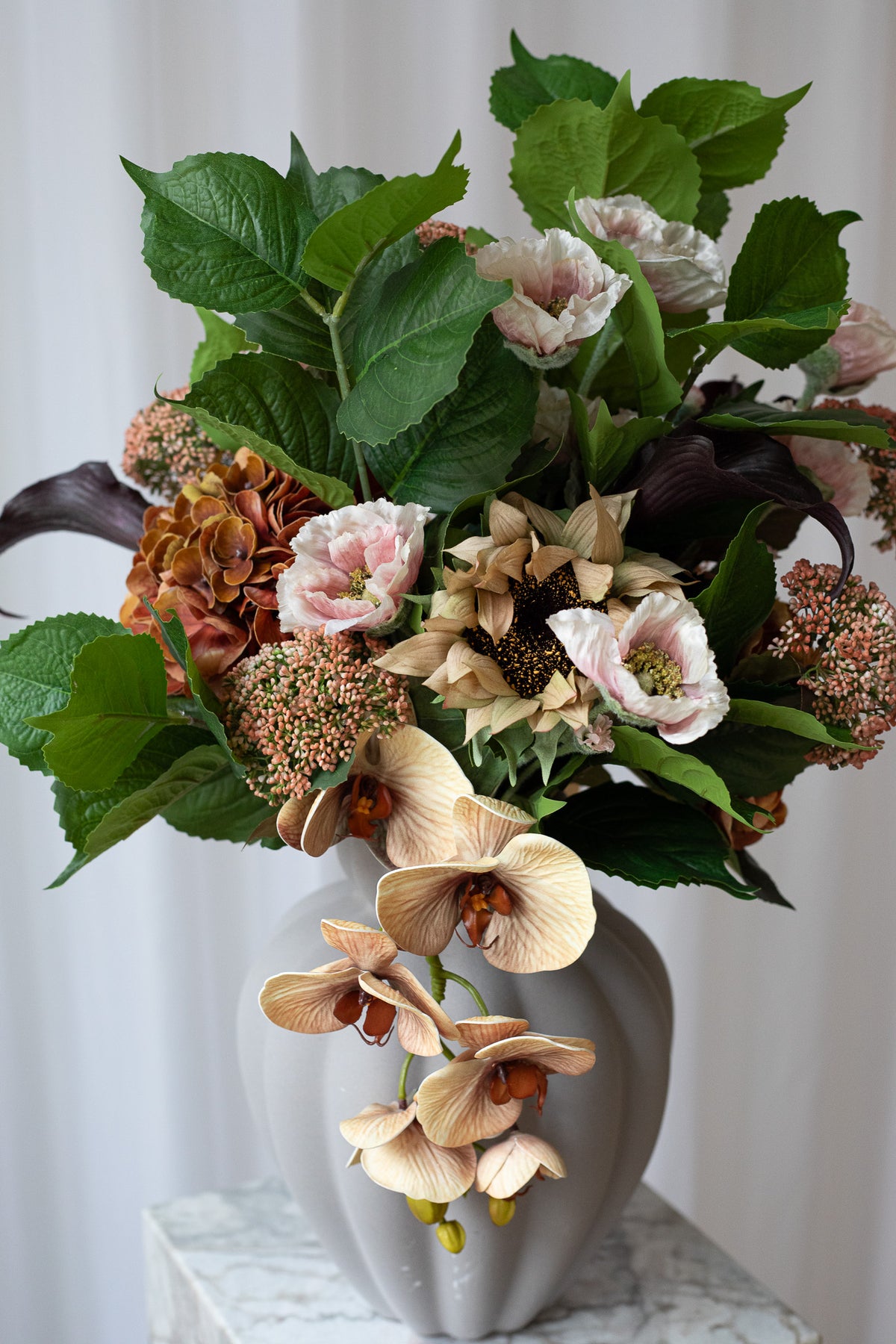 Nærbillede af kunstig buket i brændte nuancer. Buketten er i smukke brændte farver og består af calla liljer, hortensia, valmuer, solsikker og bladgrønt.