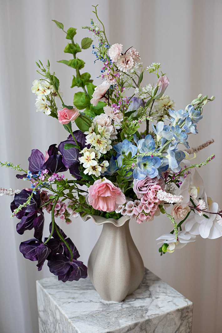 Kunstig buket af naturtro blomster i farverige nuancer.