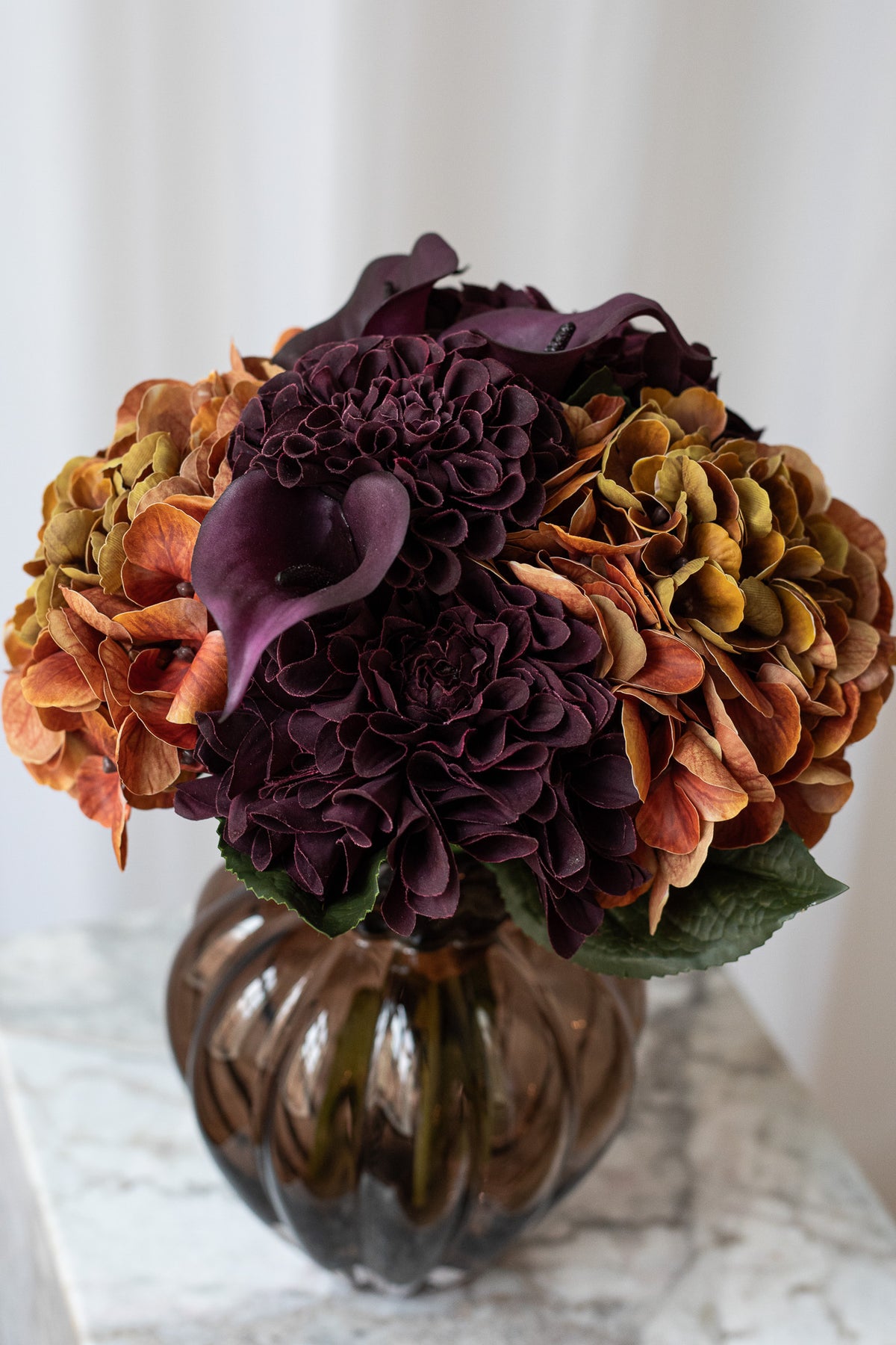 Nærbillede af kunstig buket i bordeaux og brændte orange farver med hortensia og calla liljer.