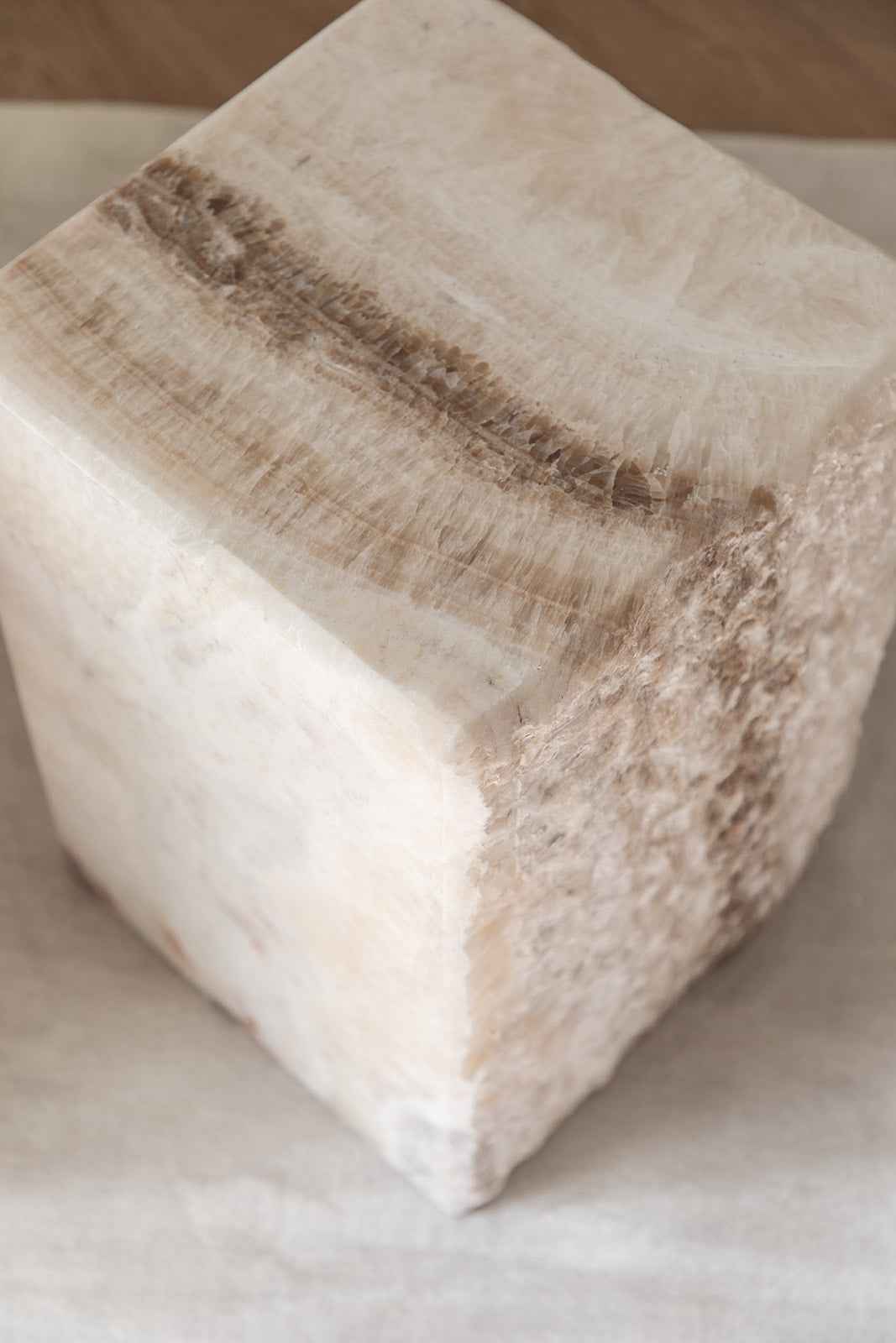 Nærbillede af en kubeformet naturstensblok med lyse nuancer og en mørkere åre gennem stenen. Overfladerne veksler mellem glatpolerede sider og rå, teksturerede kanter.