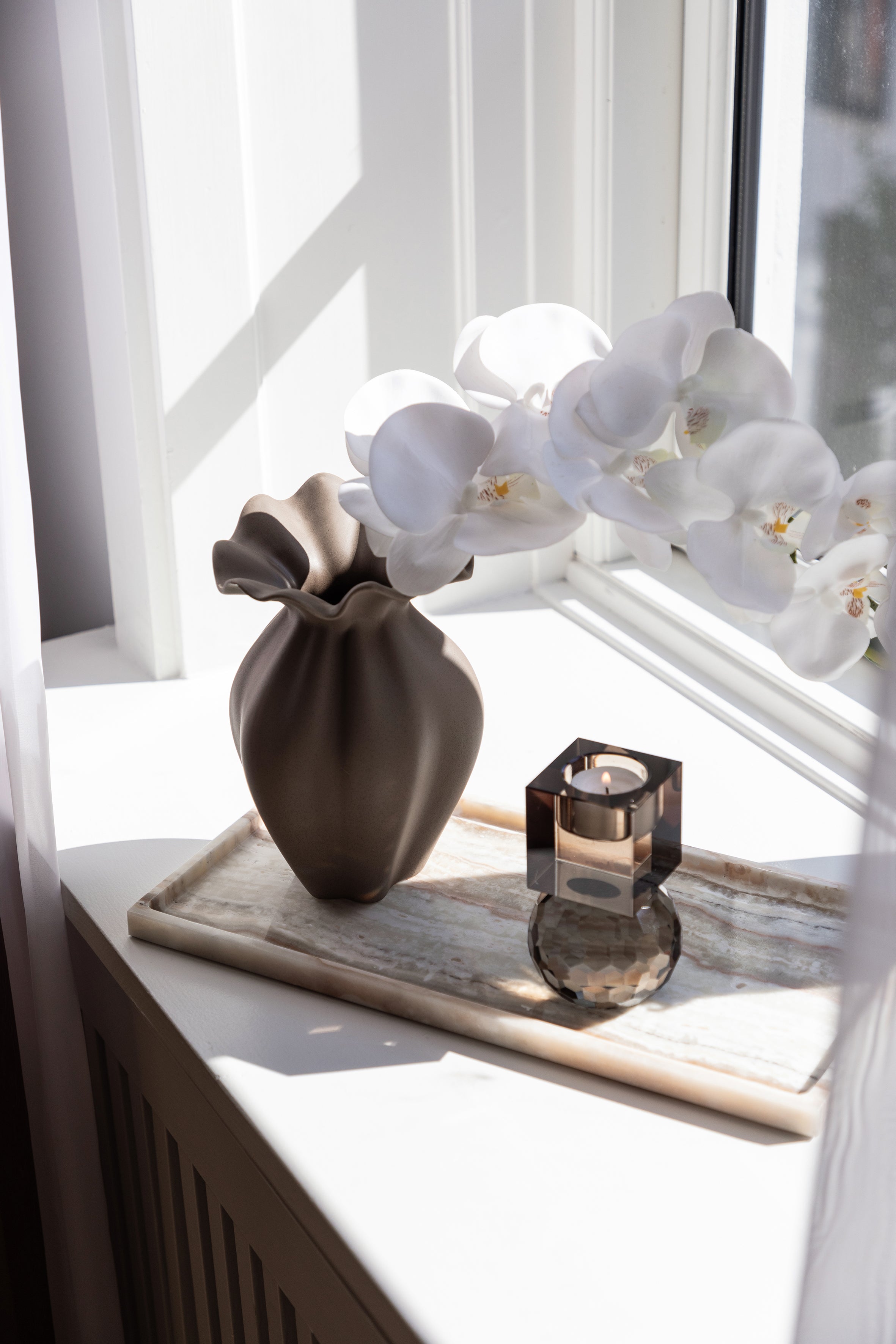 Organisk og skulpturel vase i brun fra Nellie kollektionen fra Specktrum. Keramikvasen er stylet på en marmorbakke med en lysestage i en vindueskarm. 