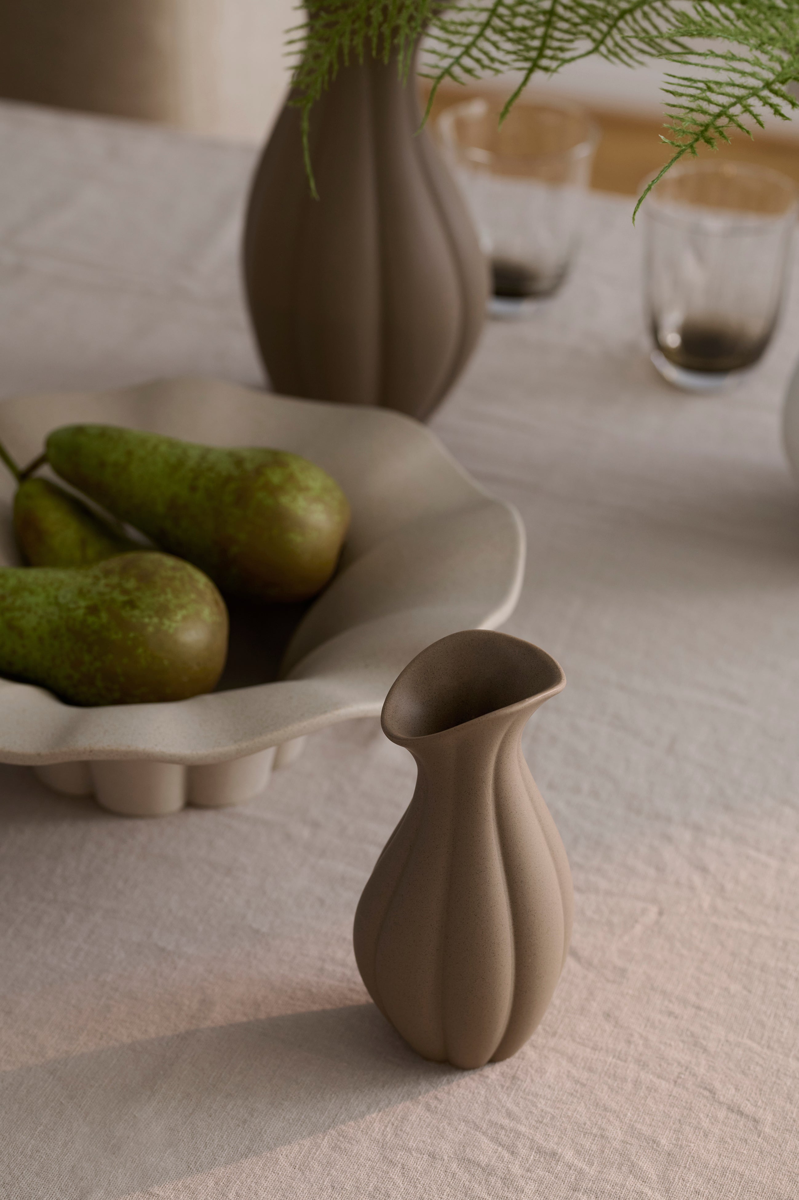 Nellie mælkekanden i brun stylet på et spisebord med andre designs fra Nellie kollektionen.