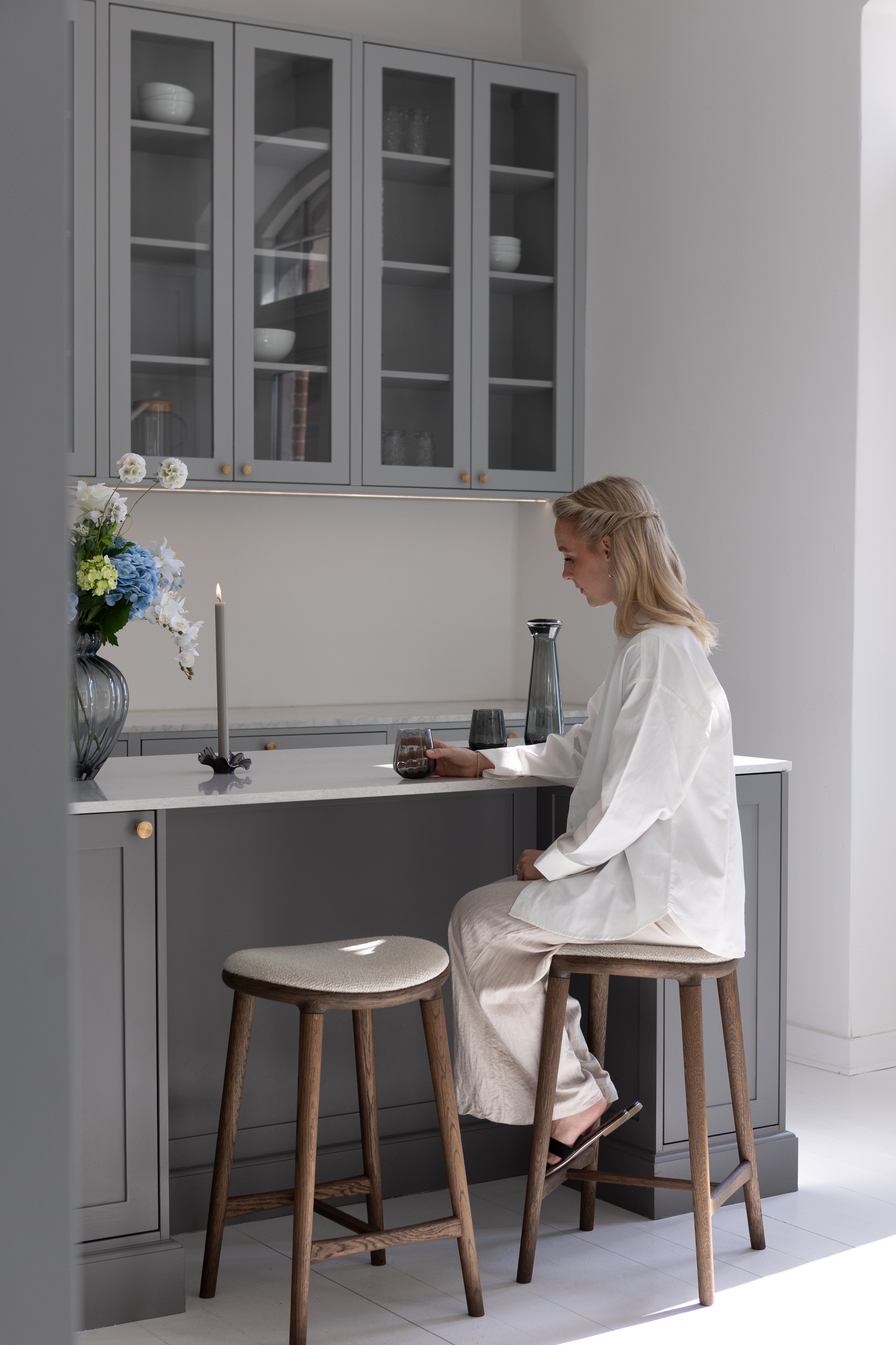 To Nohr barstole i mørkolieret eg med hvid boucle. Stolene er placeret ved en køkkenø.